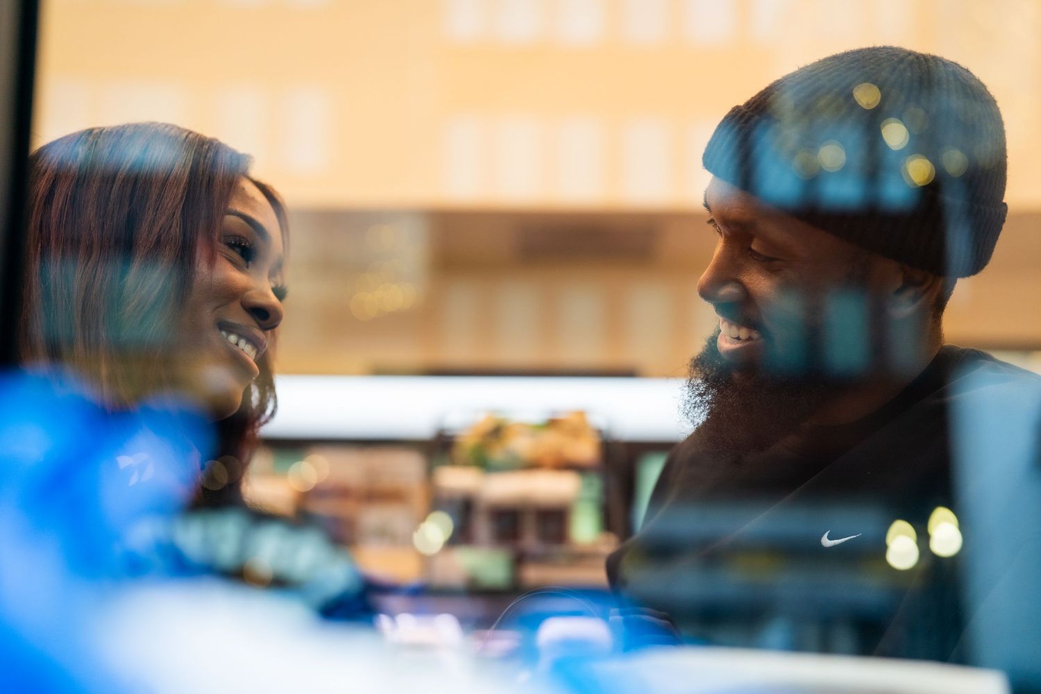 Couple smiling at each other reflected through a window with bokeh lights background.