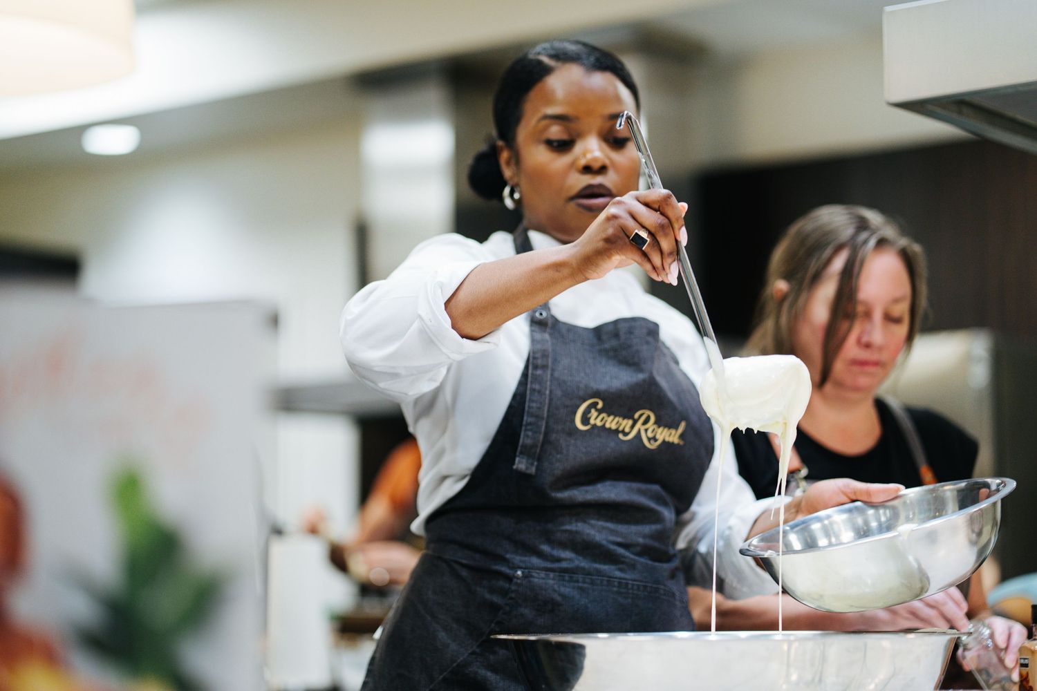 Chef in Crown Royal apron pours cream into a mixing bowl during a cooking class.