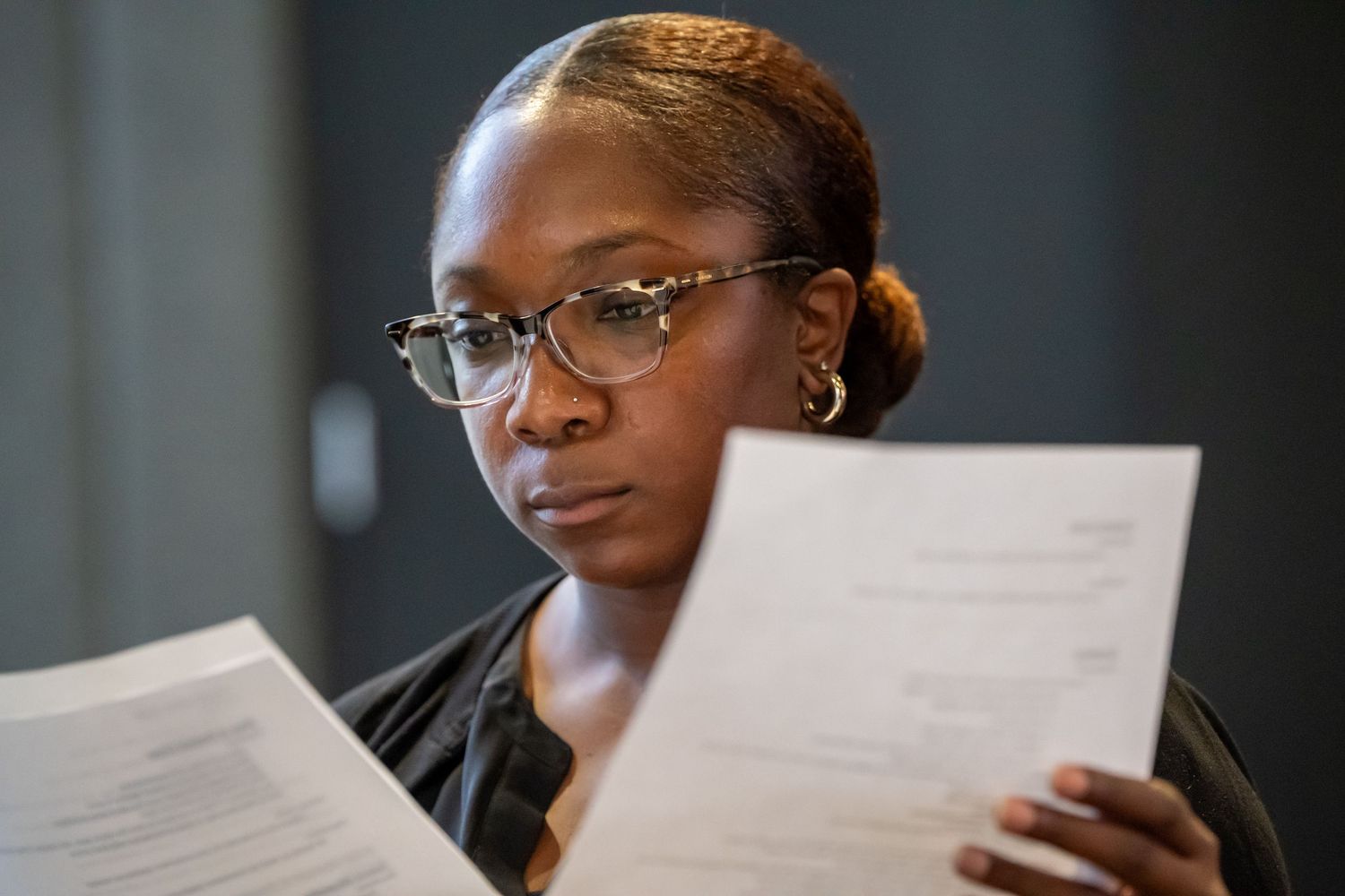 Woman with glasses carefully reviewing printed documents at a professional workshop.