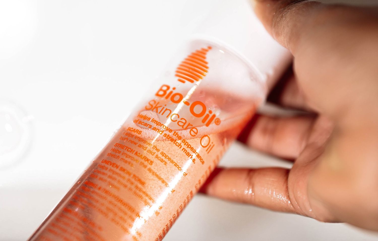 Close-up of hands holding and examining a Bio-Oil Skincare Oil orange plastic bottle.