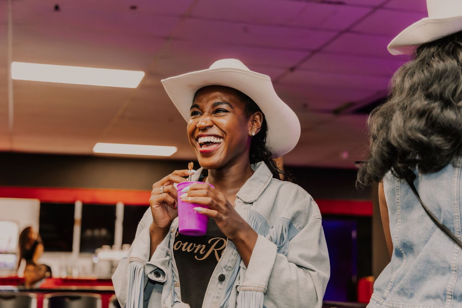 A smiling woman in a white cowboy hat enjoys a drink at a Crown Royal branded event.