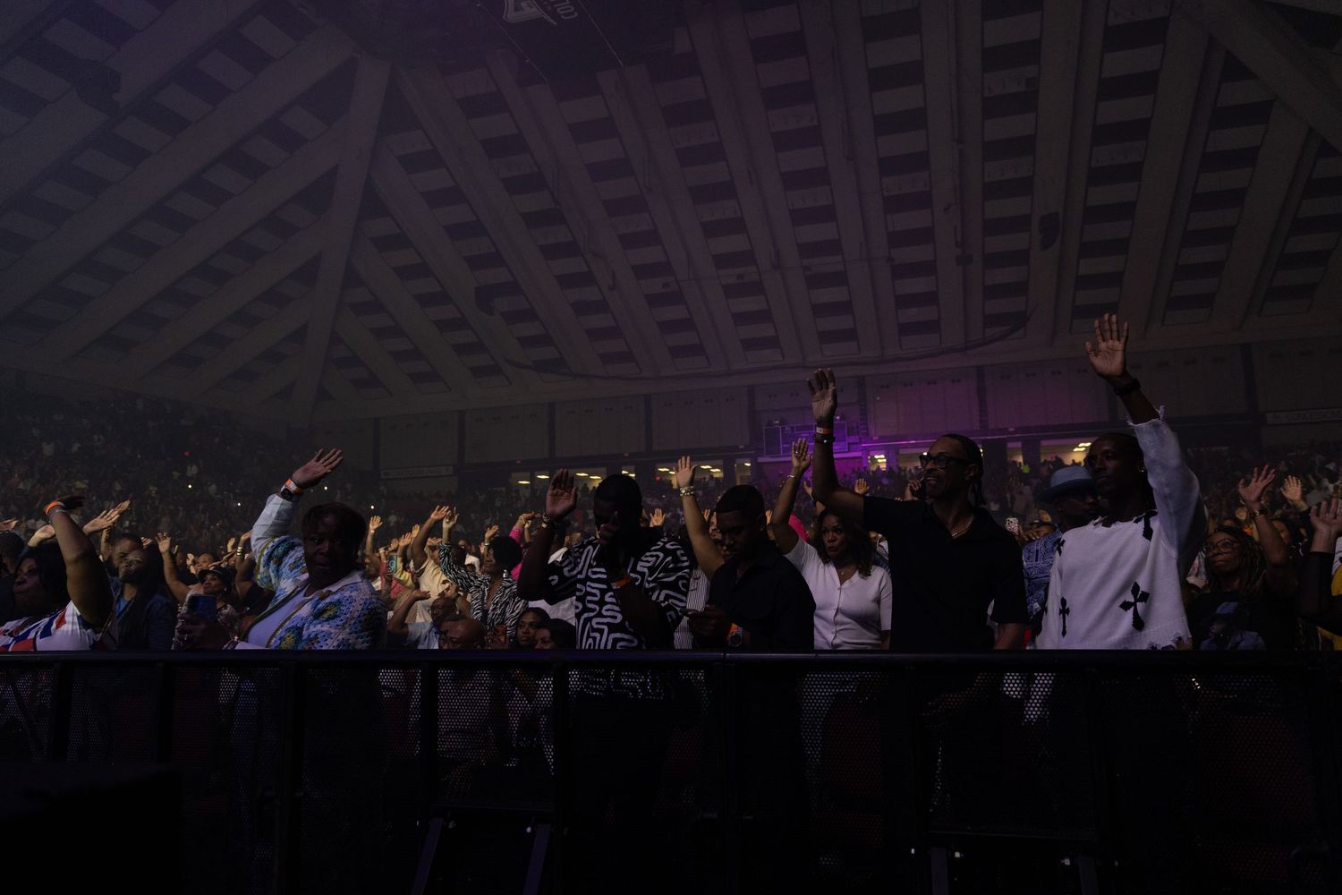 Large concert audience with hands raised under arena lighting during a live performance.
