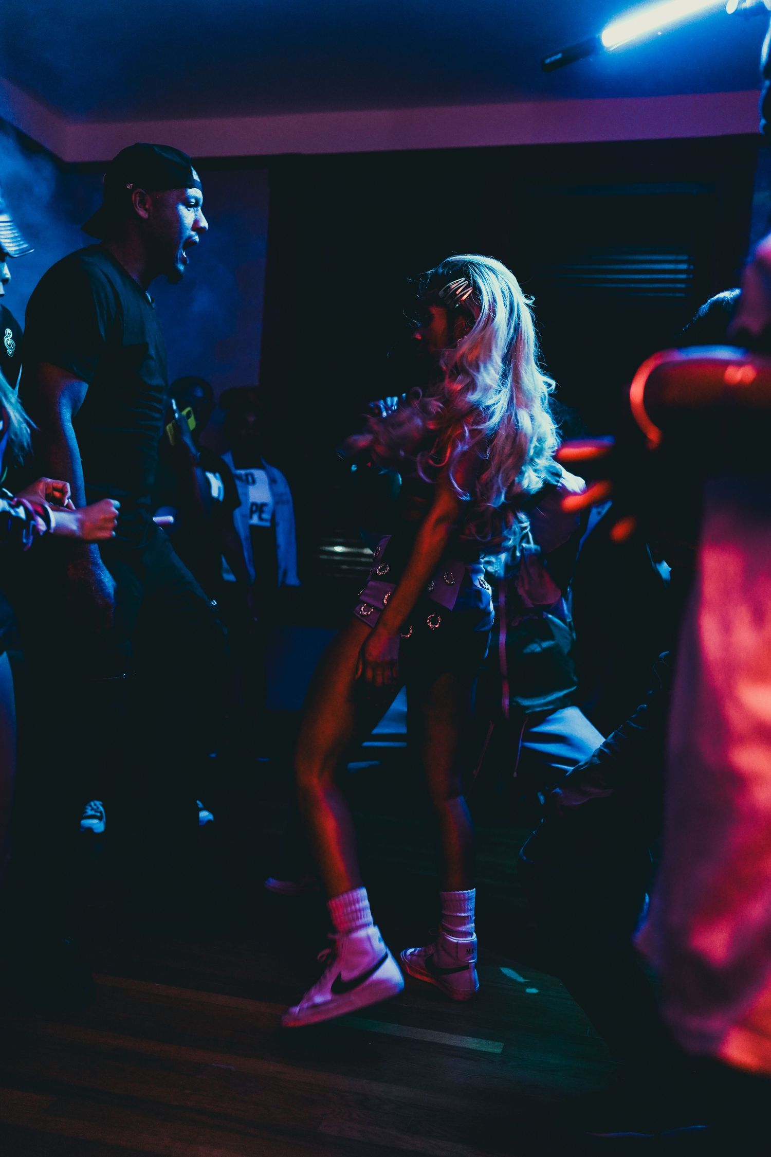 A woman with blonde hair dances under blue neon lights at a nightclub music video shoot.