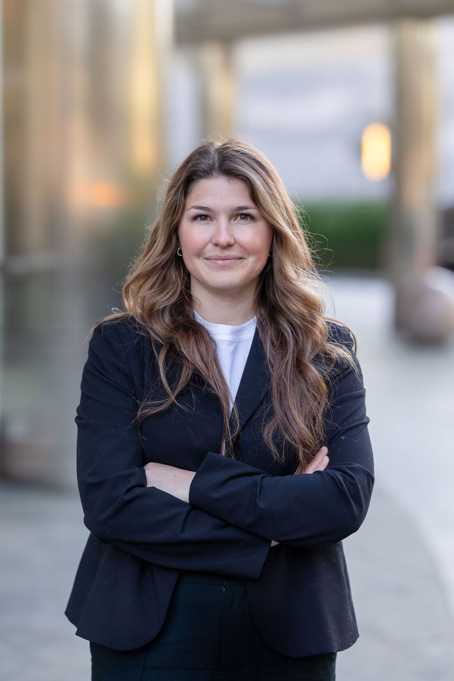 Professional in a dark business suit stands confidently with arms crossed.