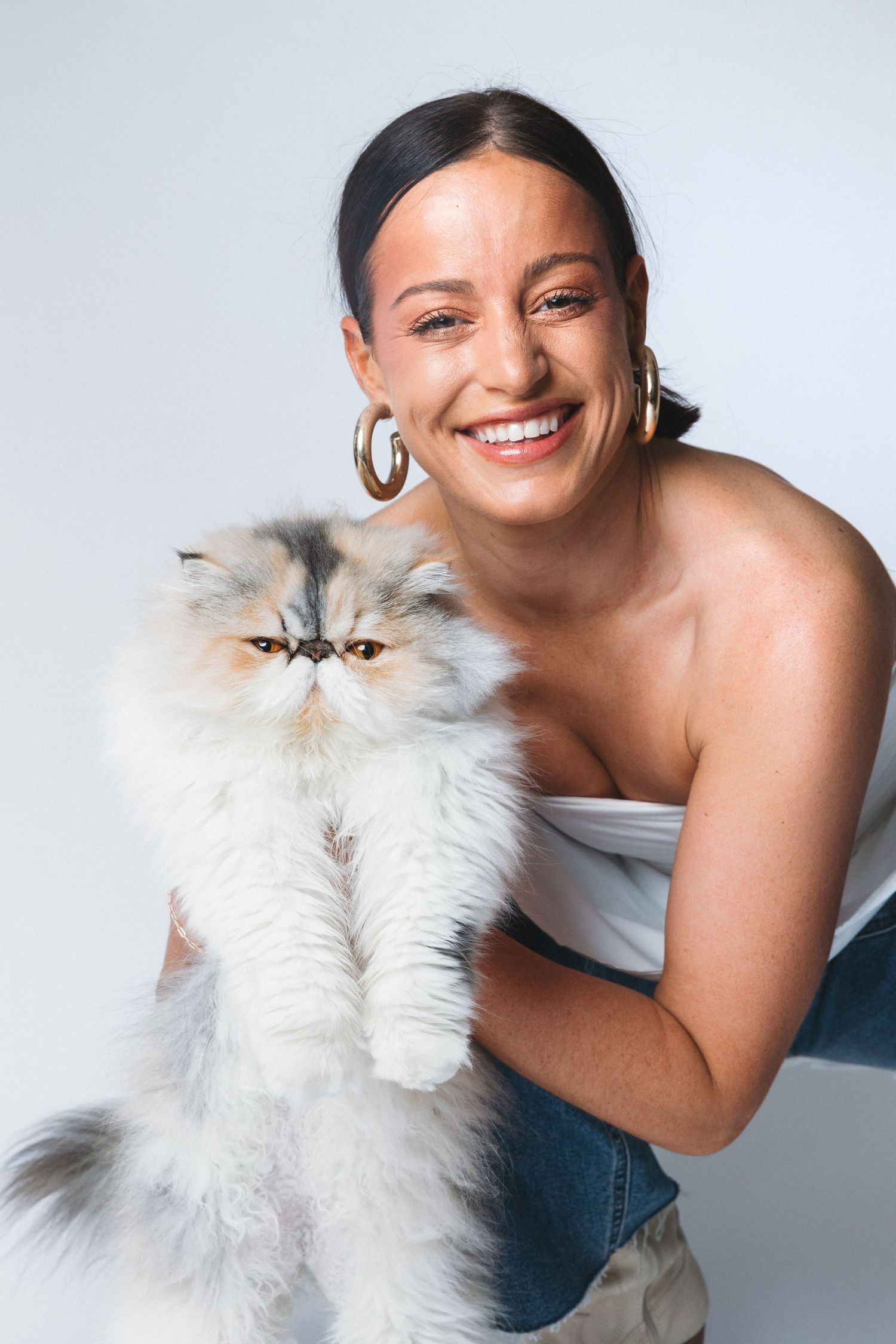 Portrait of someone holding a fluffy white Persian cat while wearing white top and denim.