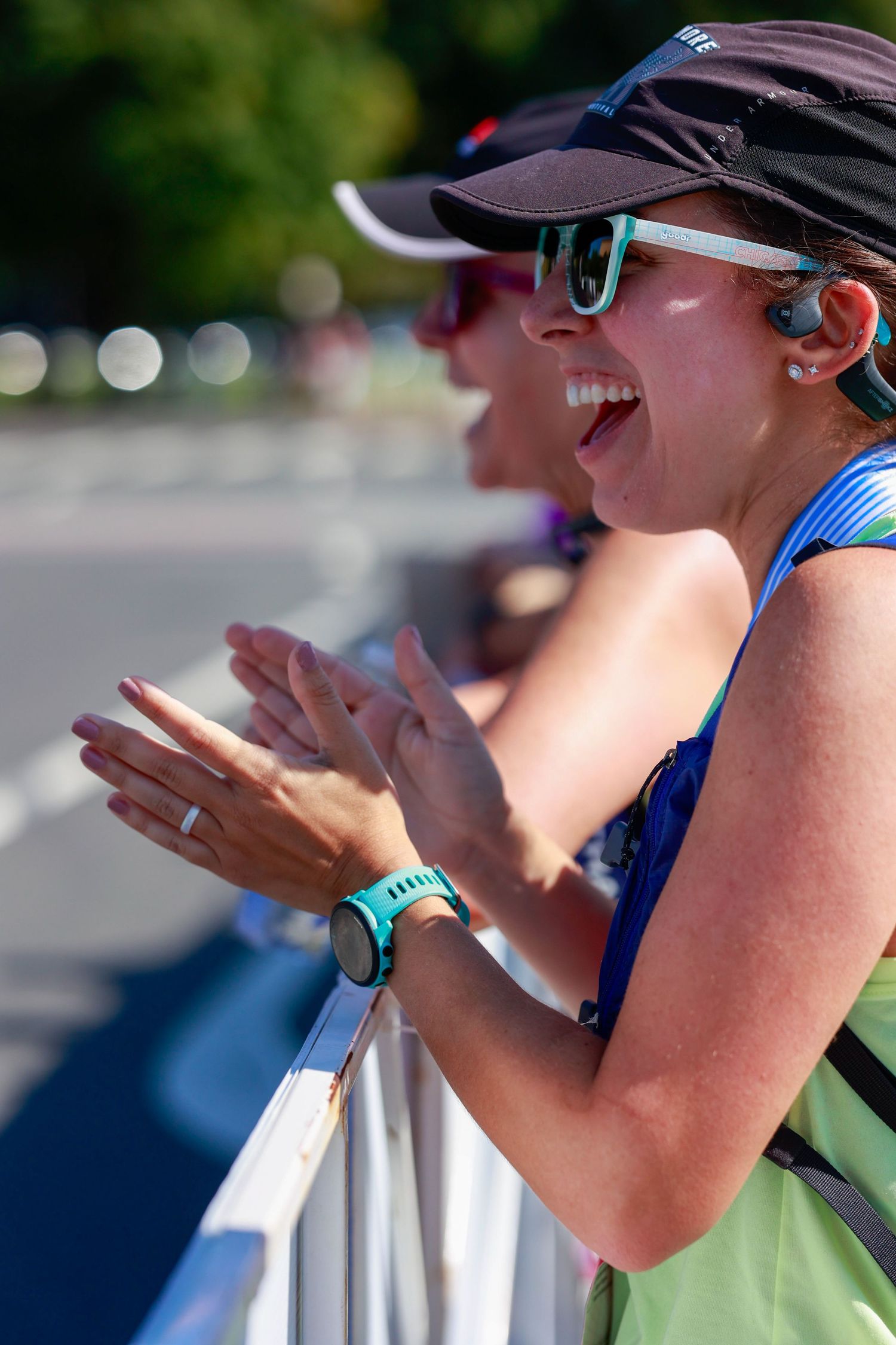 Enthusiastic spectator in sunglasses and baseball cap cheering at outdoor sporting event.