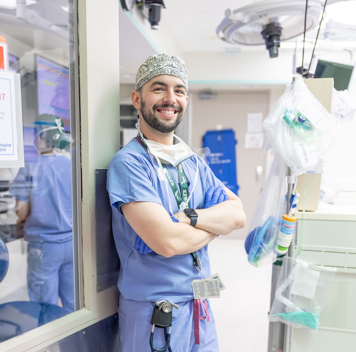 Medical professional in blue scrubs and surgical cap smiling in a hospital corridor.
