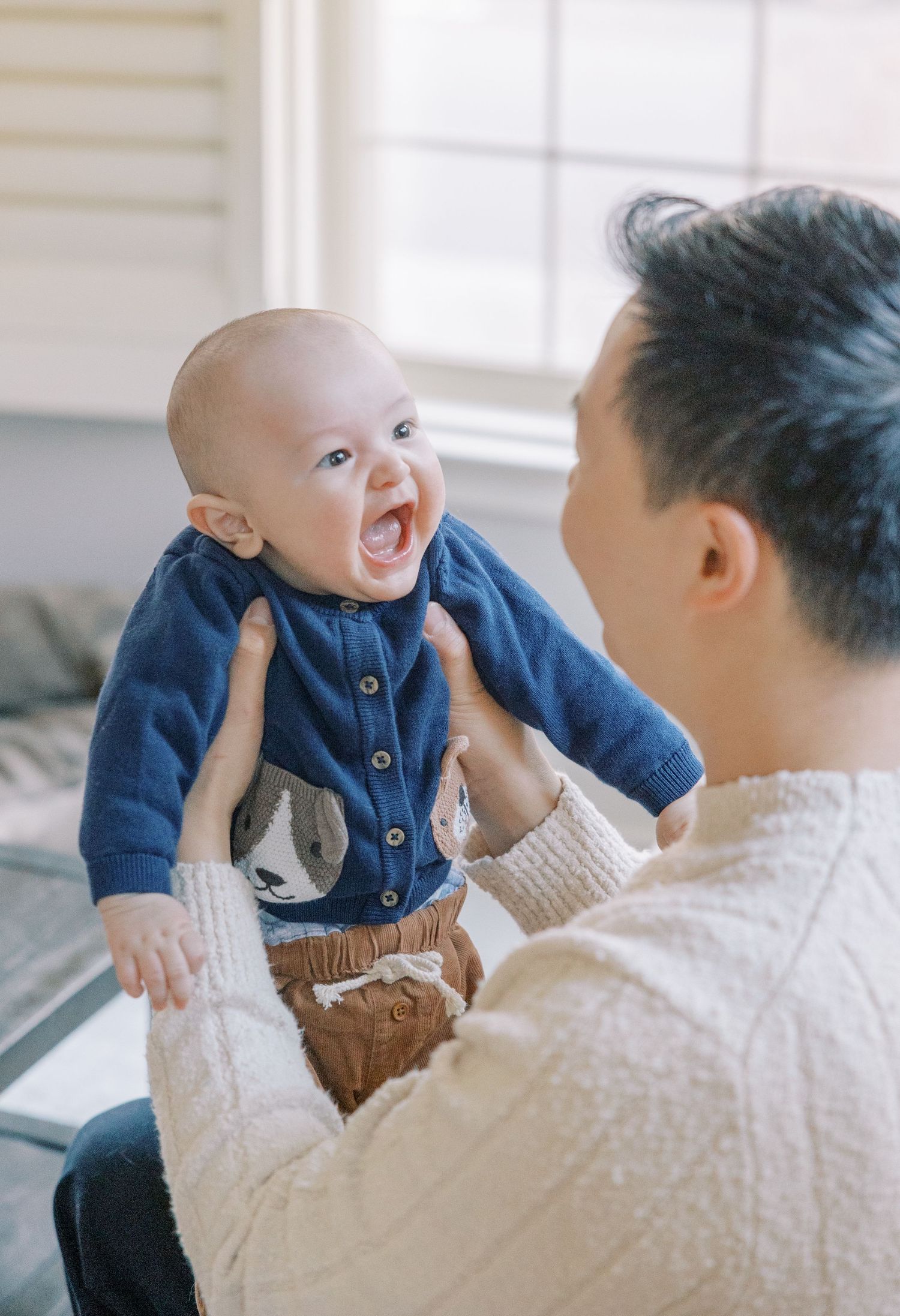 Tender moment between parent and baby wearing blue cardigan indoors.