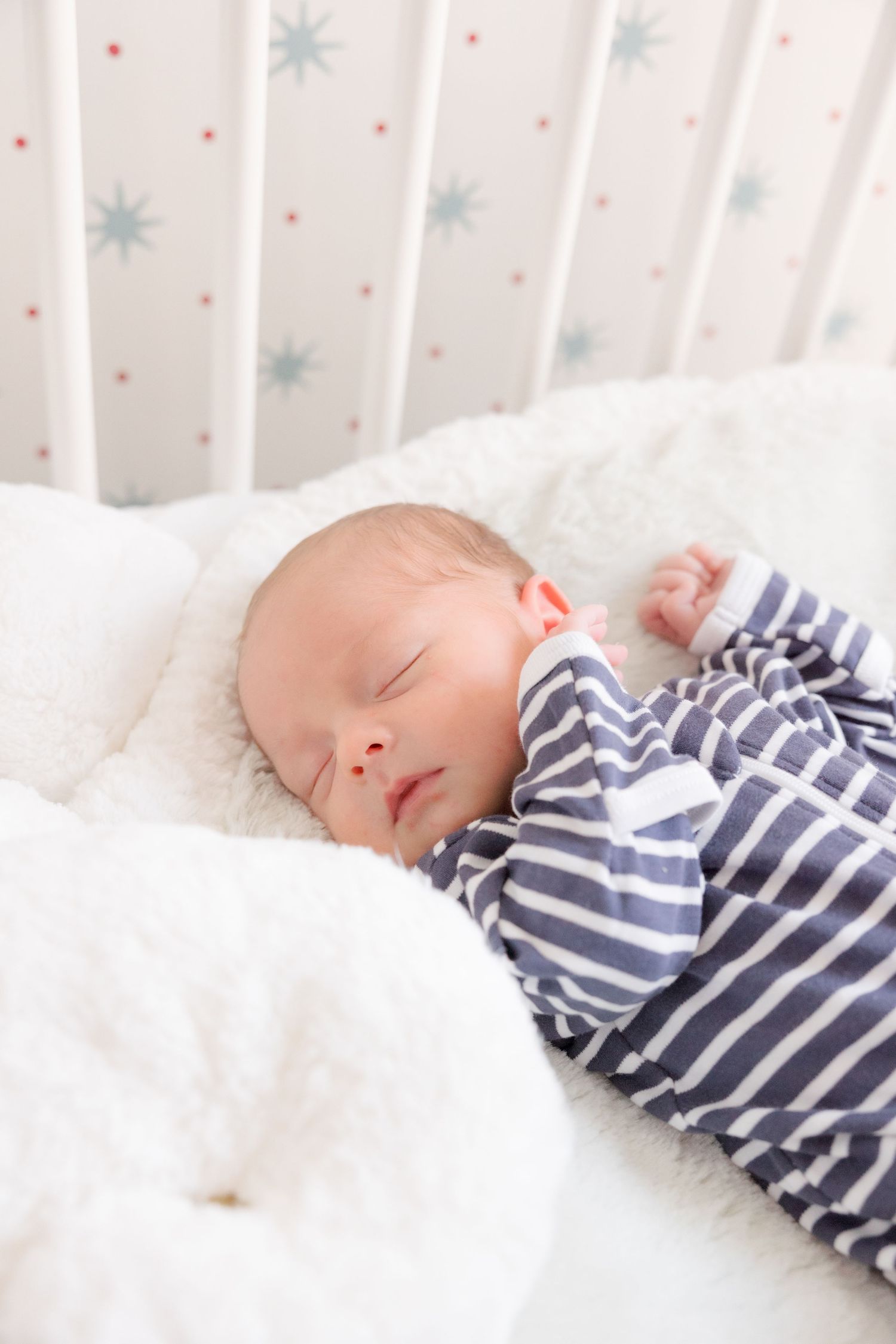 A sleeping baby wearing navy and white striped pajamas rests peacefully on white bedding.
