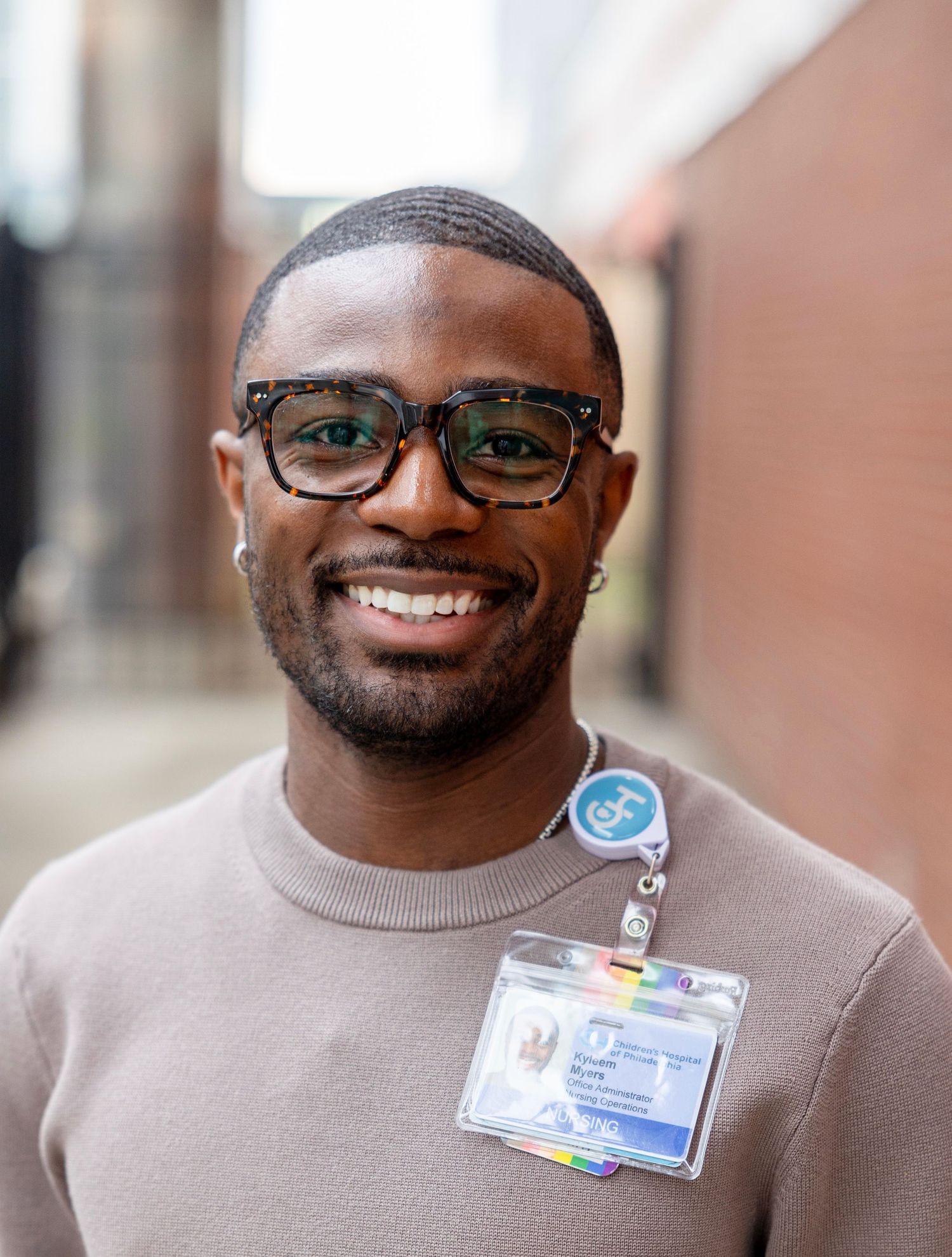 Healthcare professional wearing glasses and a brown sweater smiles warmly at the camera.