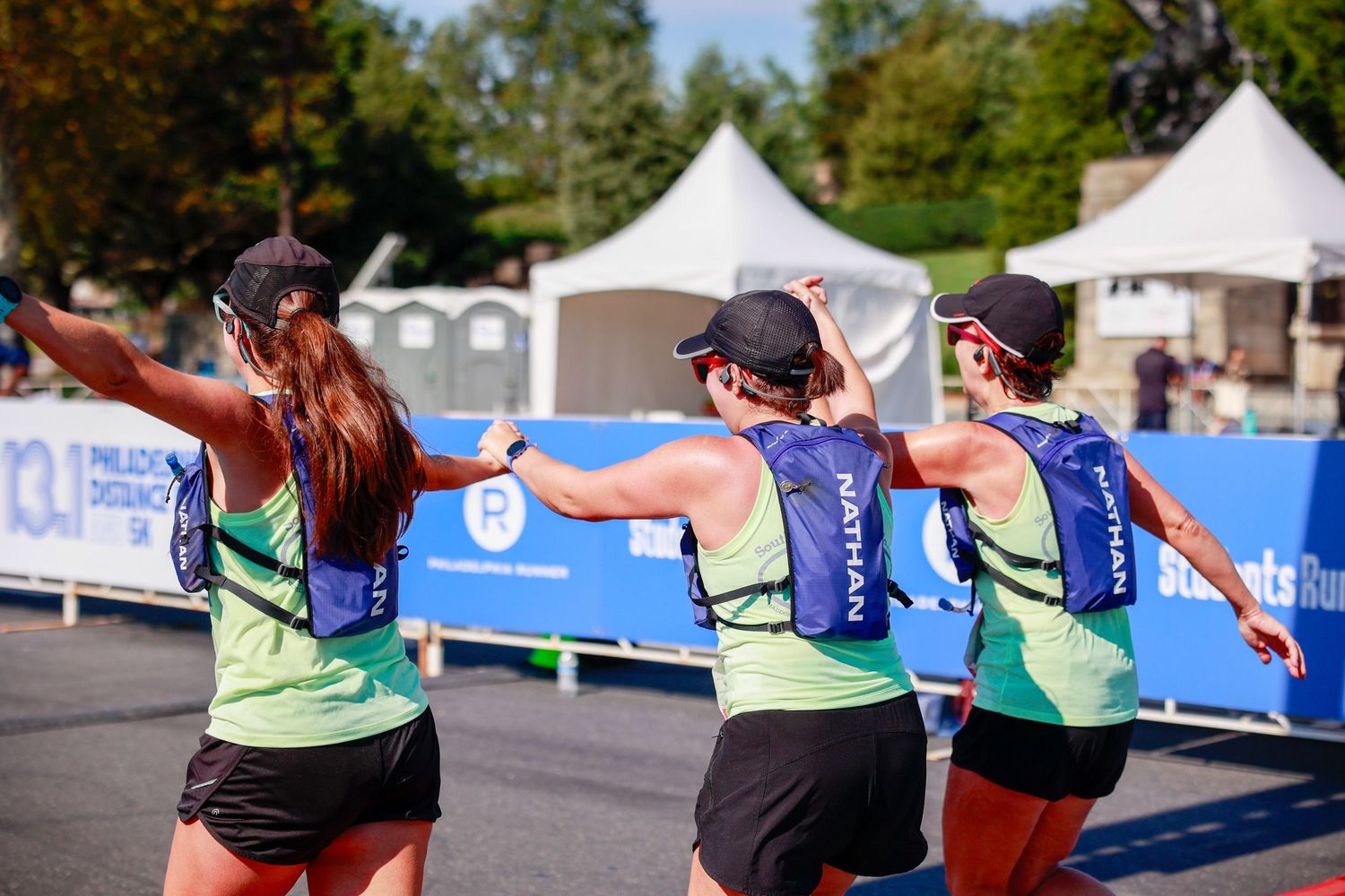Three runners in matching uniforms celebrating together at a race finish line.