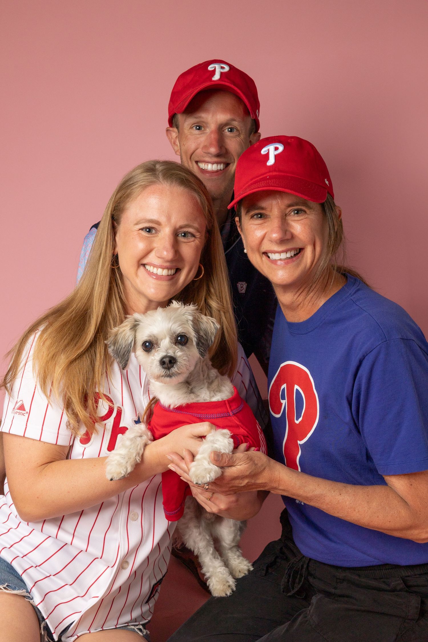 Family wearing Philadelphia Phillies gear poses with small white dog in matching baseball outfit.