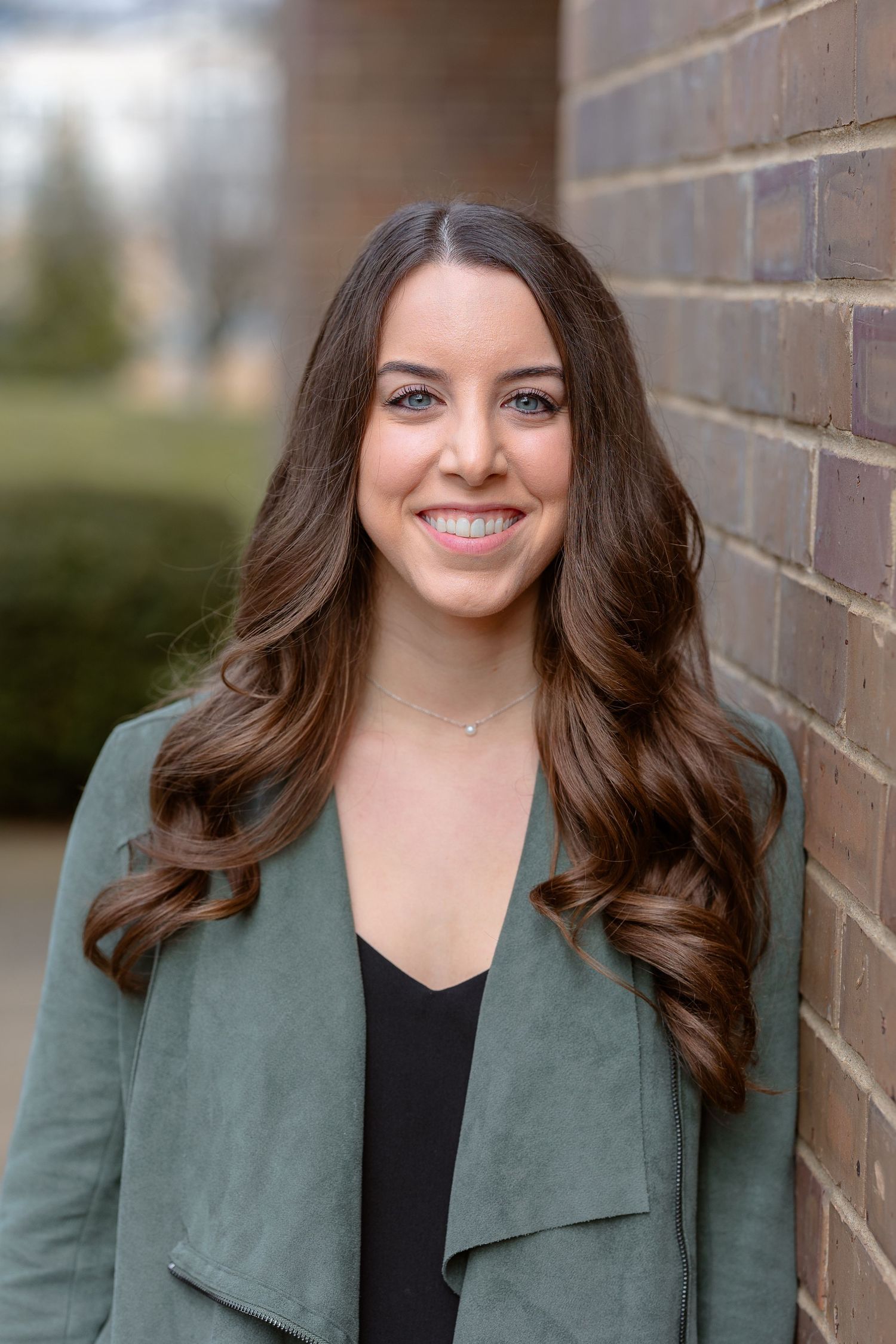 Professional headshot series against brick background with warm natural smile.