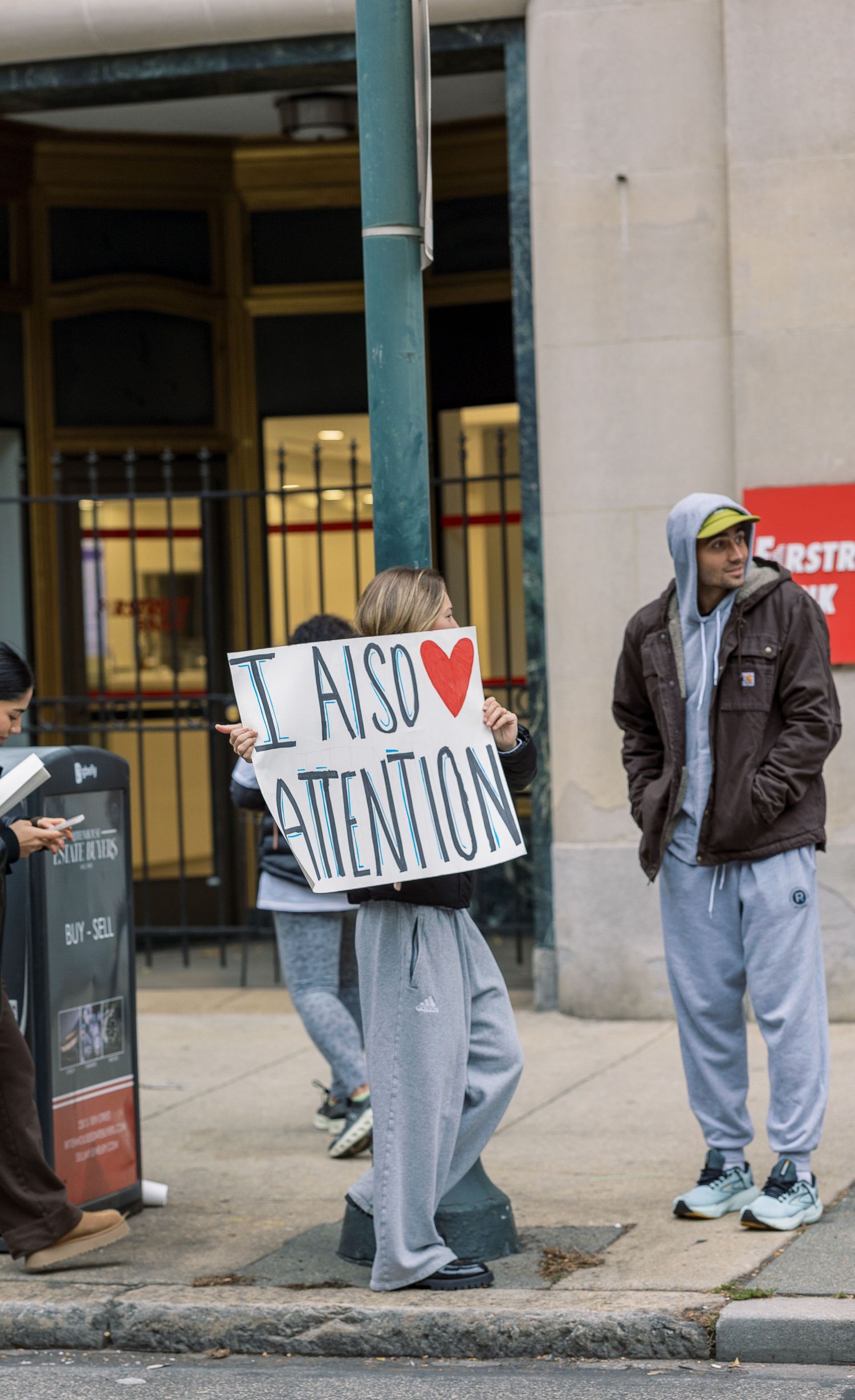 Spectators hold signs and wait along an urban street during a marathon event.