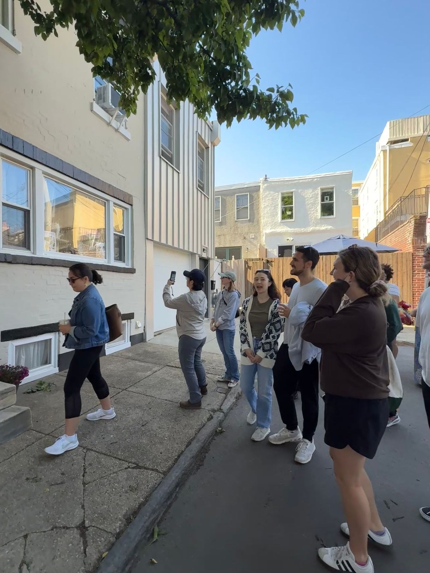 Group of people gathered on a narrow urban alley between rowhouses during a neighborhood walking tour.