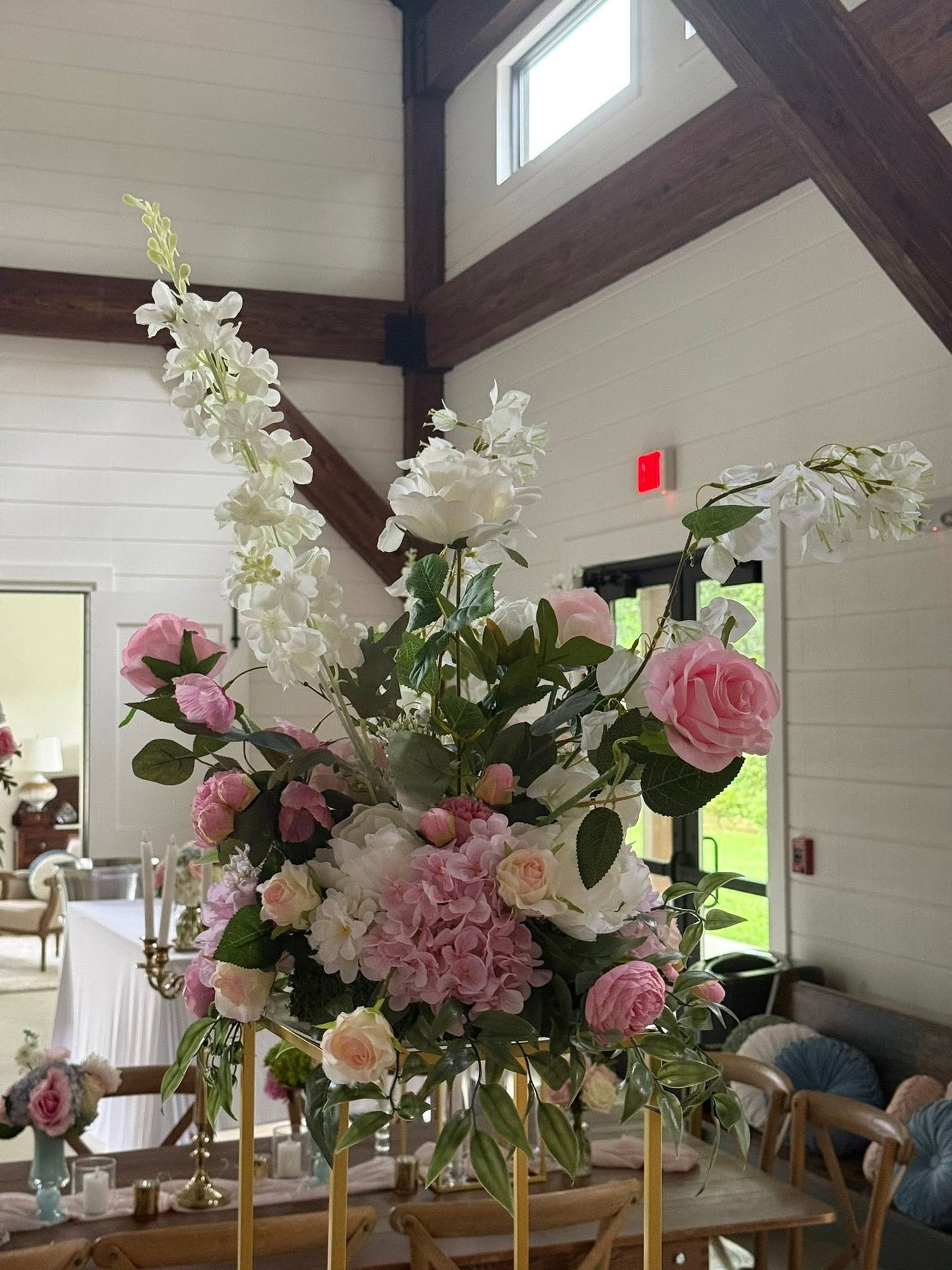 Tall floral centerpiece with pink roses, hydrangeas, and white blooms on gold stand in elegant barn venue.