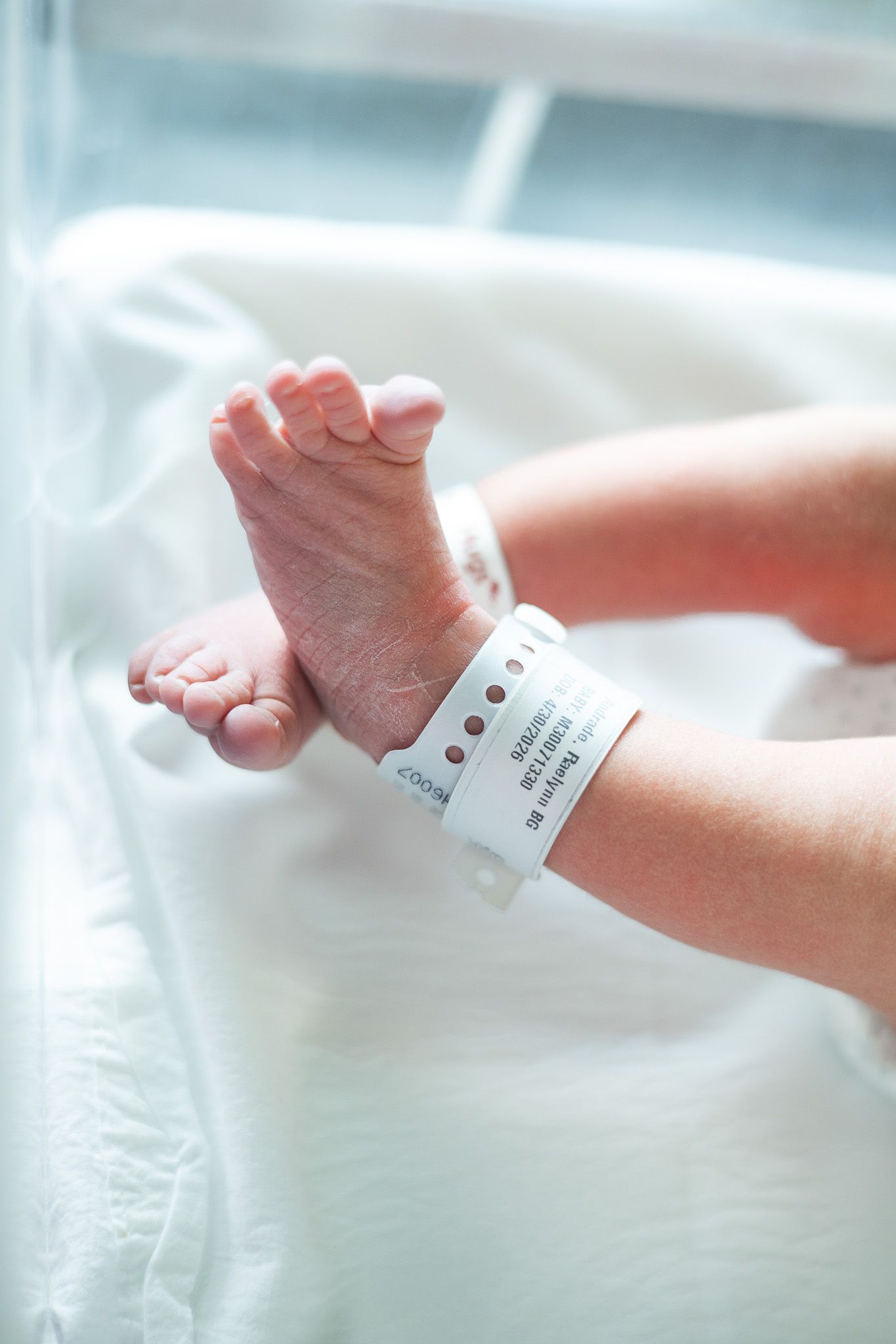 Newborn baby feet with hospital identification bracelet in a white bassinet after birth.