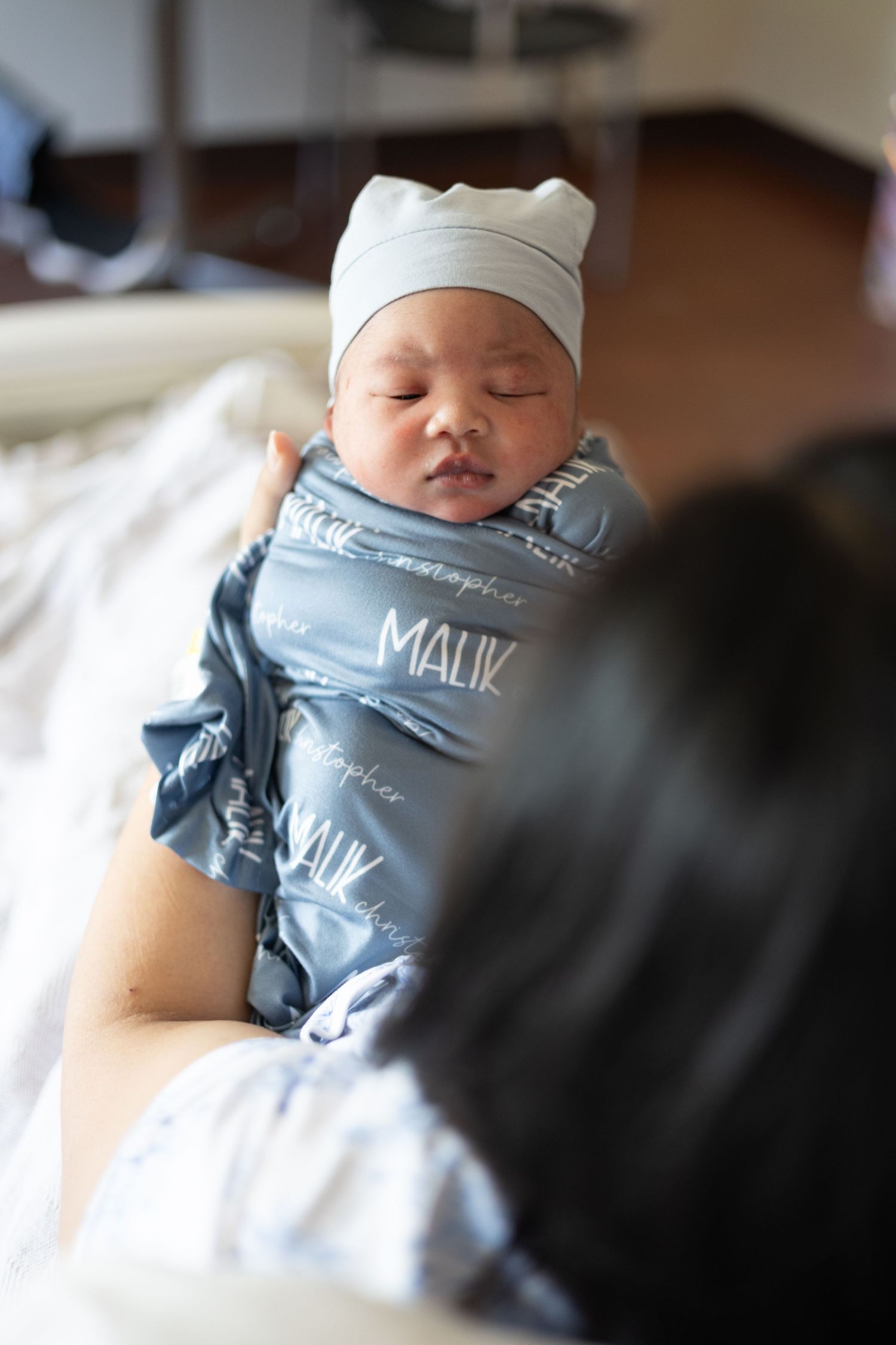 Newborn baby named Malik swaddled in personalized blue blanket with knit hat in hospital.