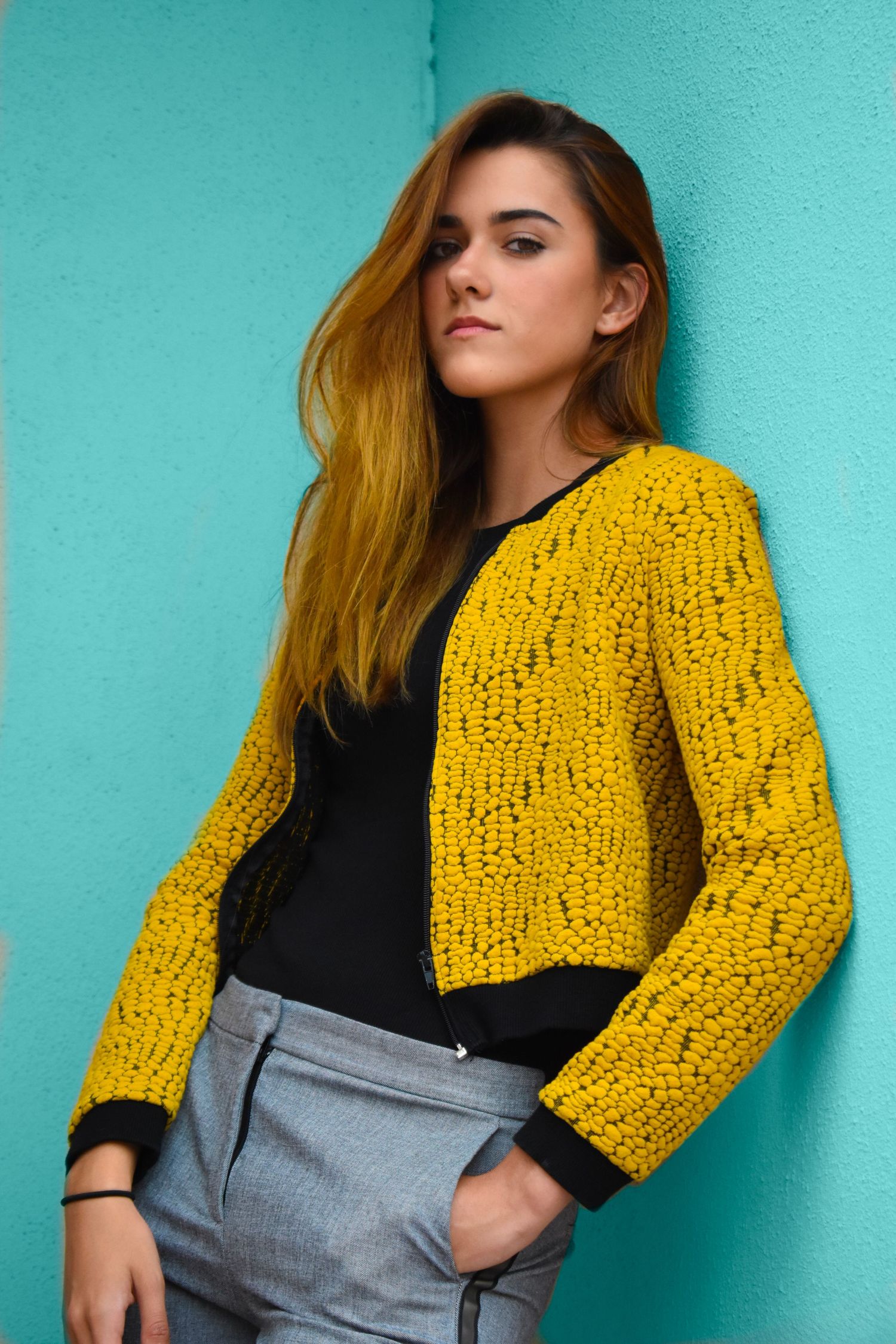 Portrait photography in Brownsville Texas of woman in yellow knit cardigan against teal wall