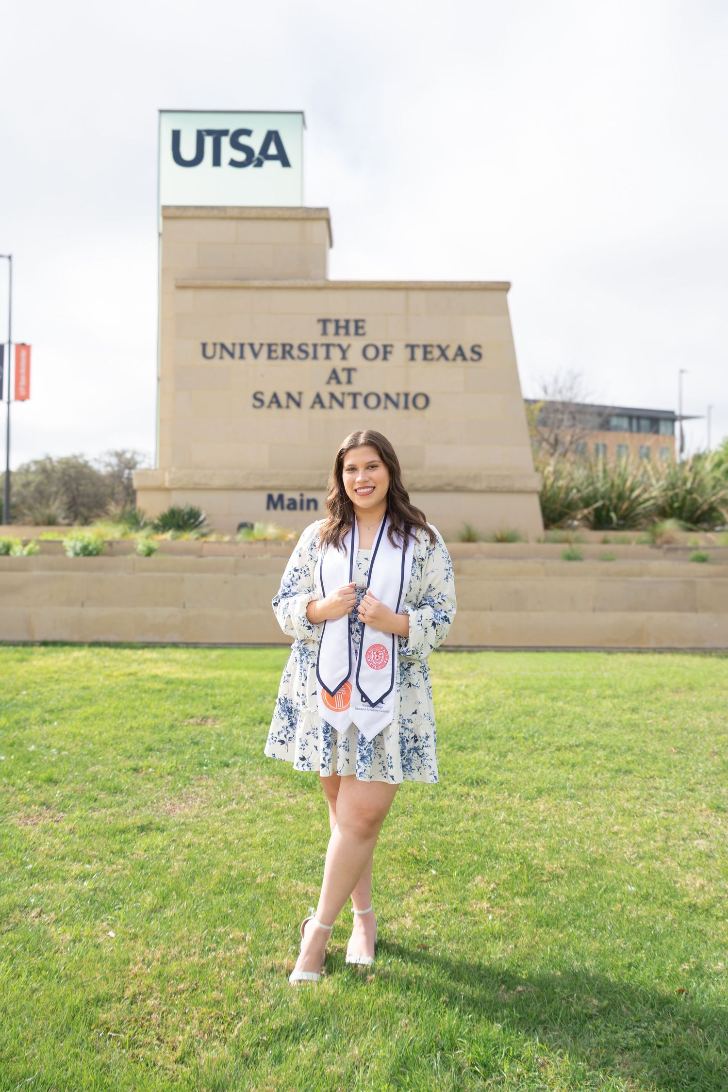 UTSA graduation portrait in front of the University of Texas San Antonio sign in floral dress