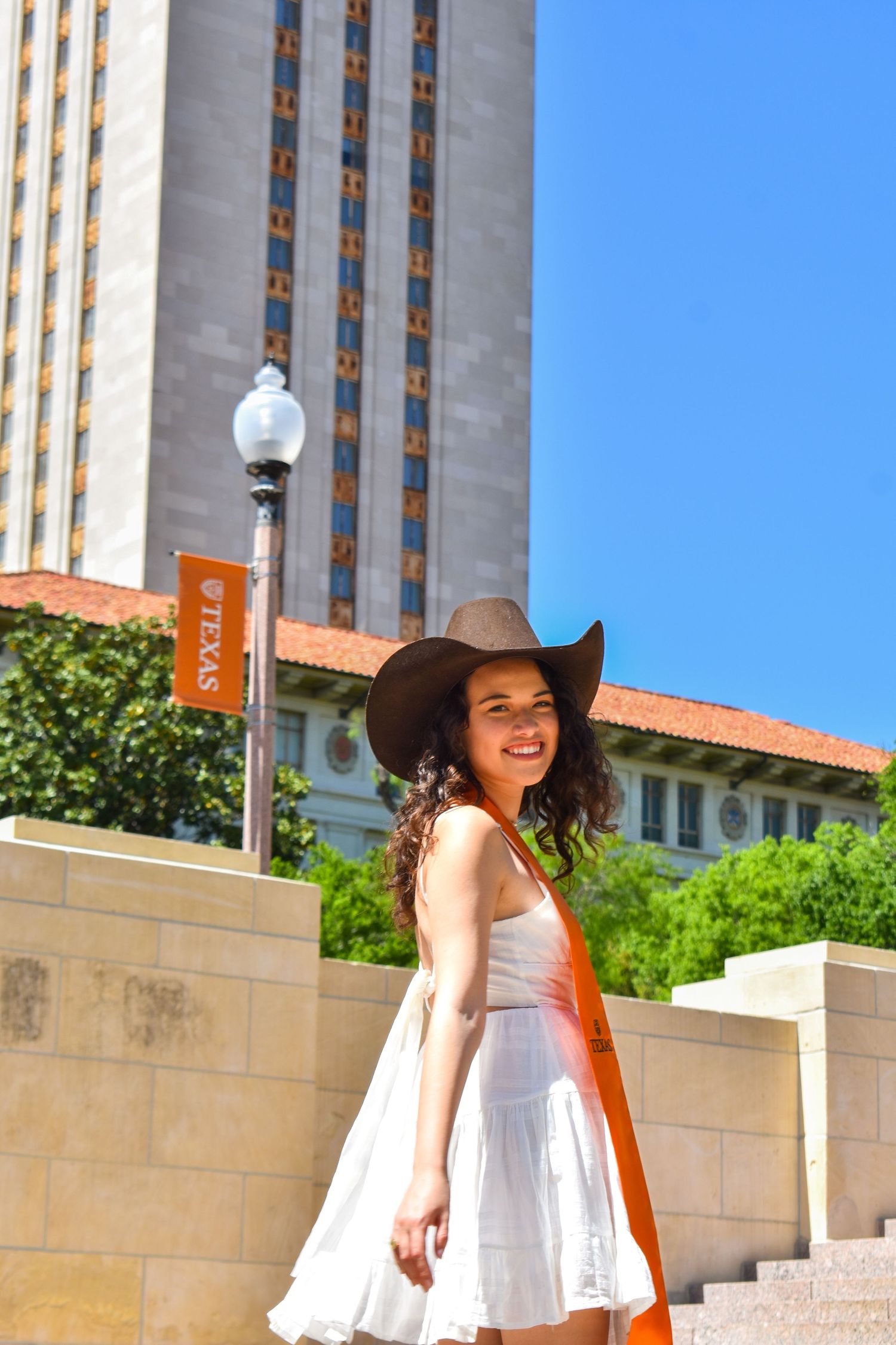UT Austin graduation portrait near the Tower with graduate in white dress and cowboy hat