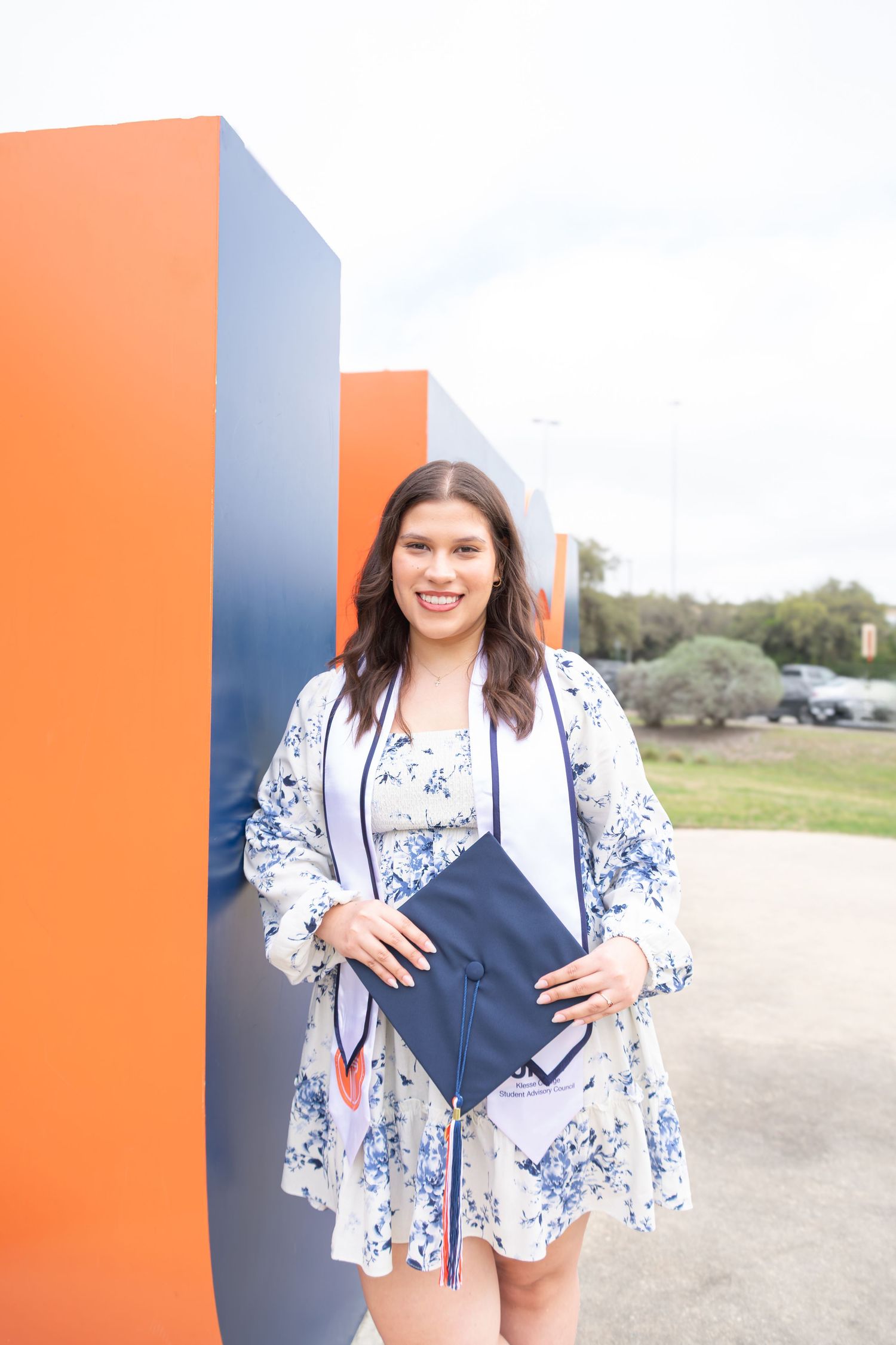 UTSA graduation portrait beside the UTSA orange letter sculpture in San Antonio with diploma