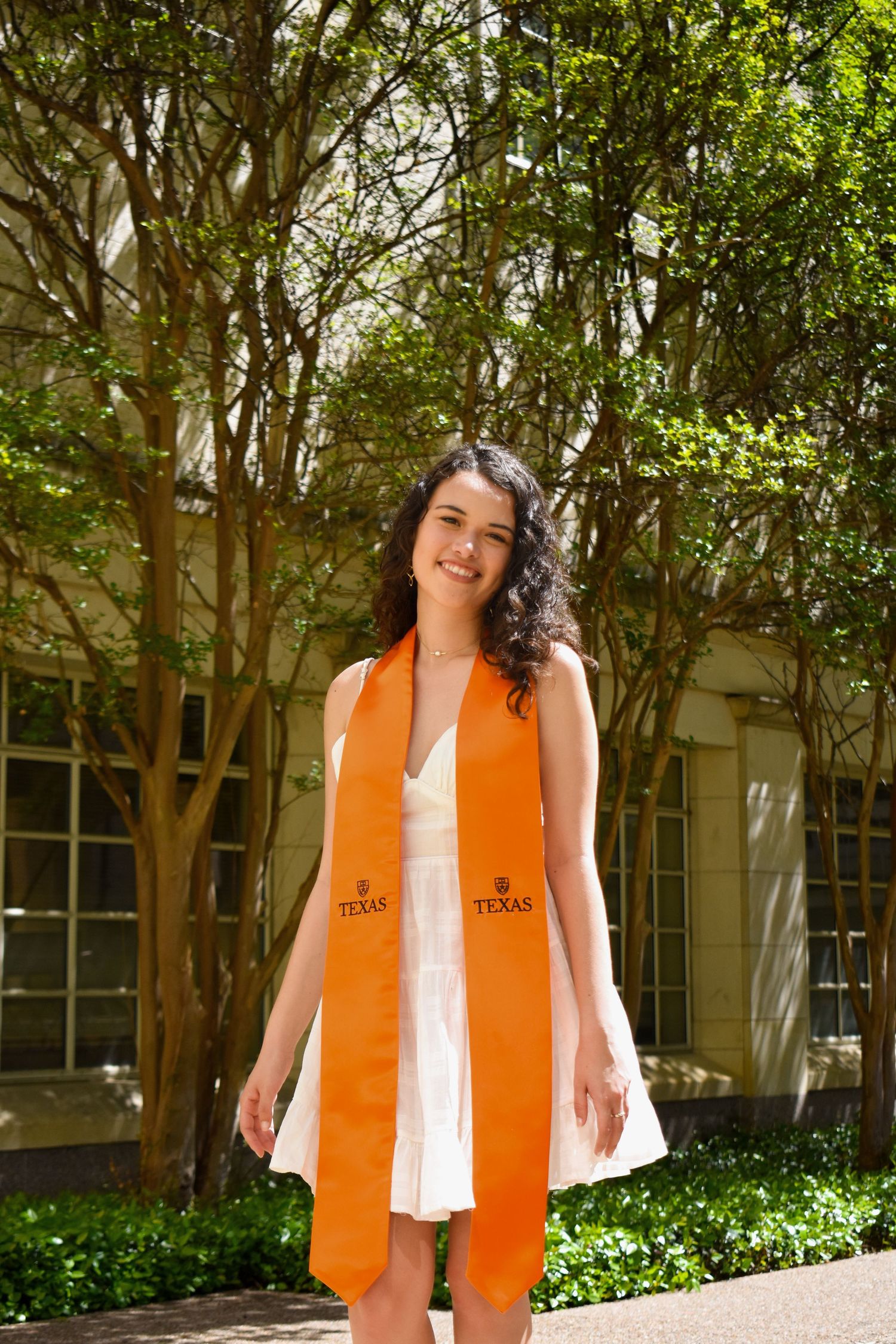 UT Austin graduation portrait outdoors on campus wearing orange Texas stole