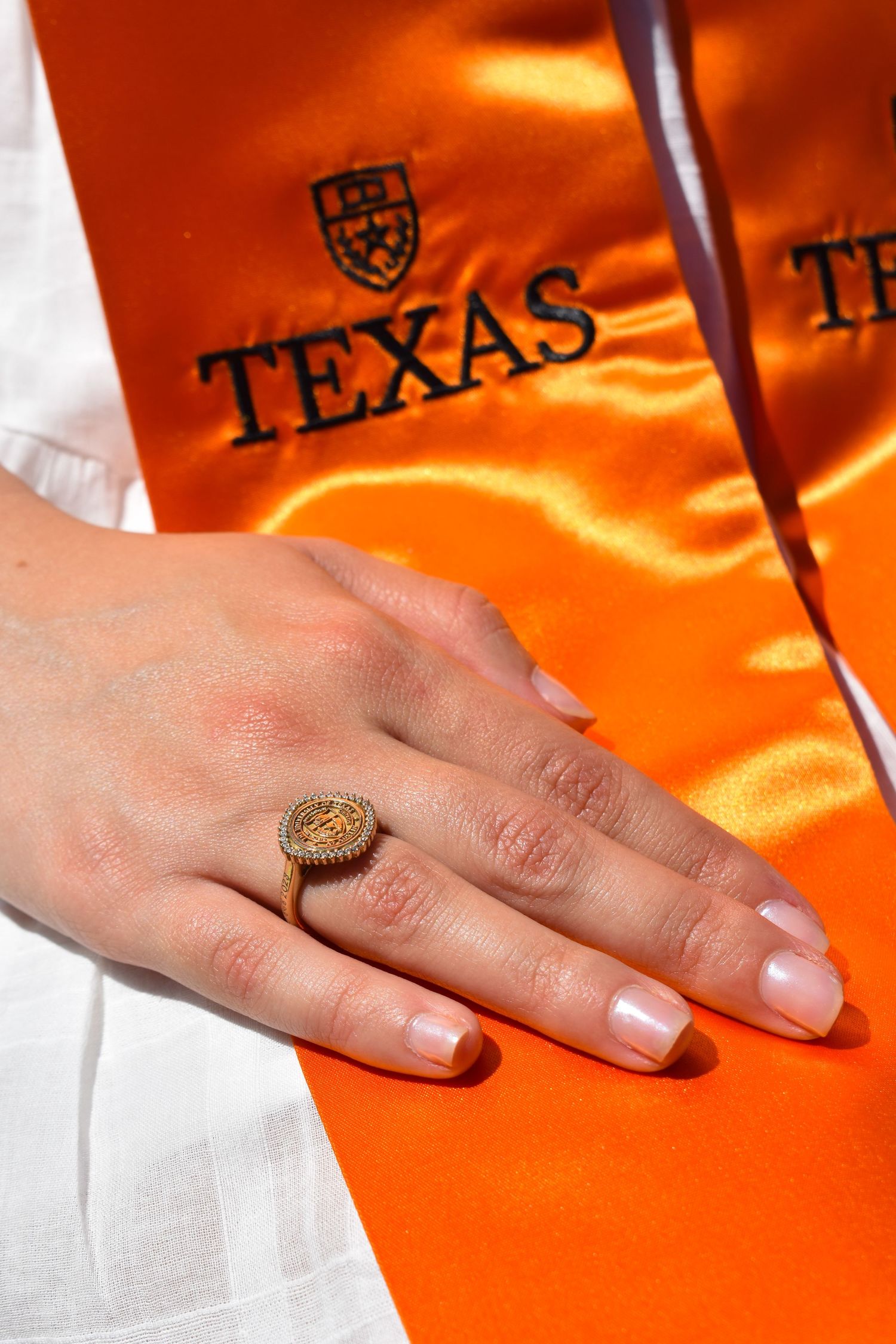 Close-up of UT Austin class ring with orange Texas graduation stole