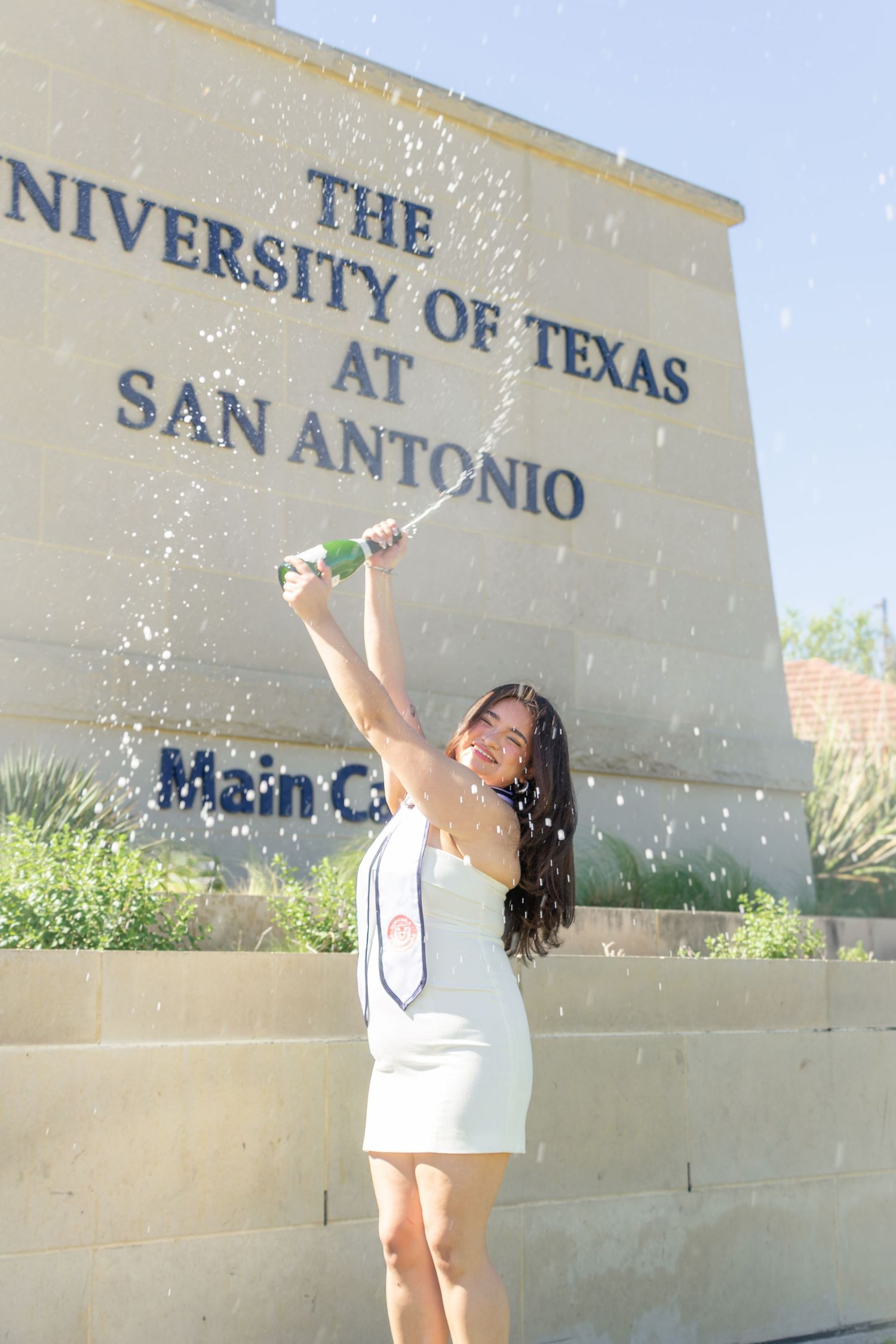 UTSA graduation portrait celebrating with confetti in front of the University of Texas San Antonio sign