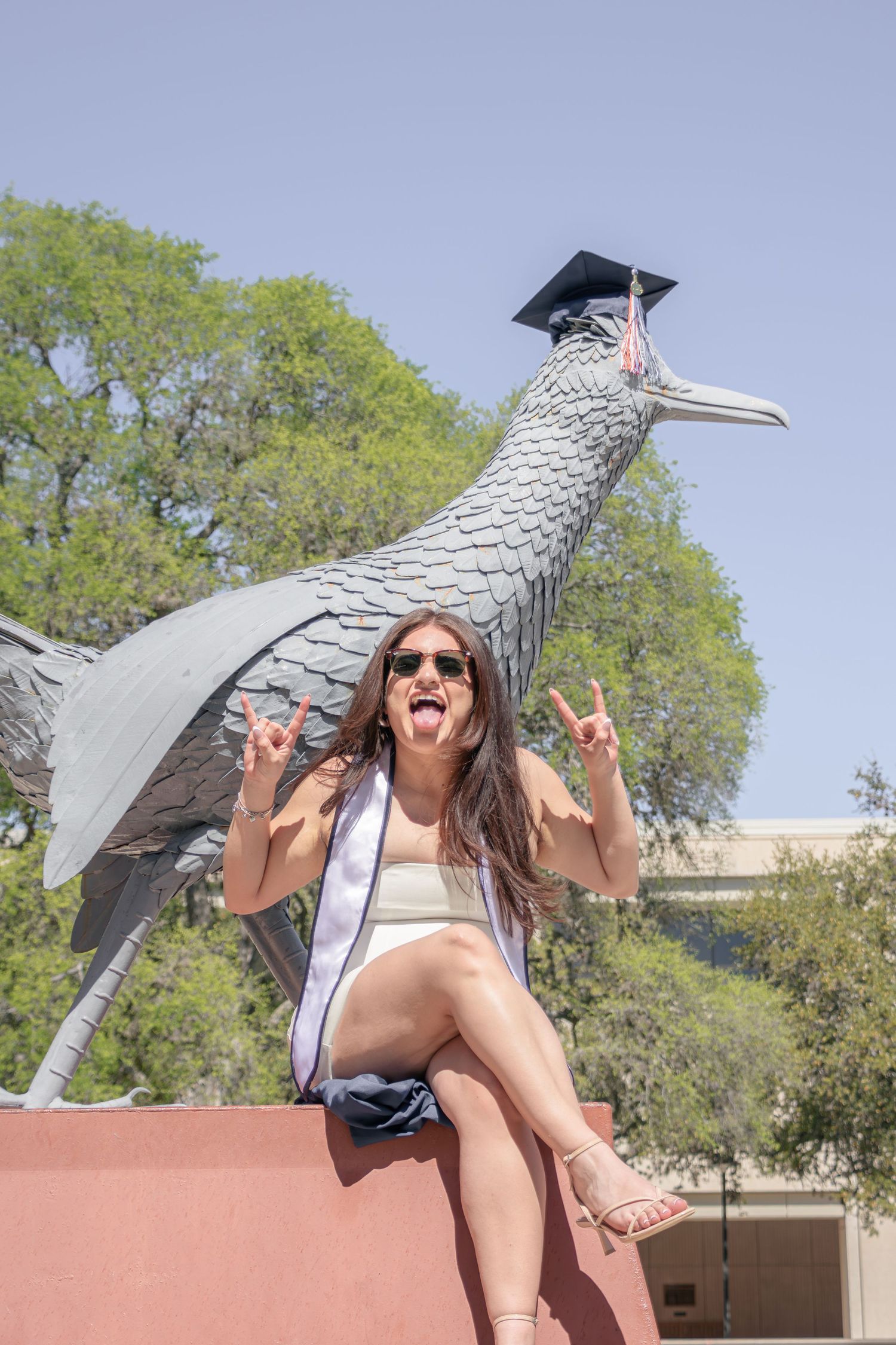 UTSA graduation portrait sitting on the Roadrunner statue on campus in San Antonio