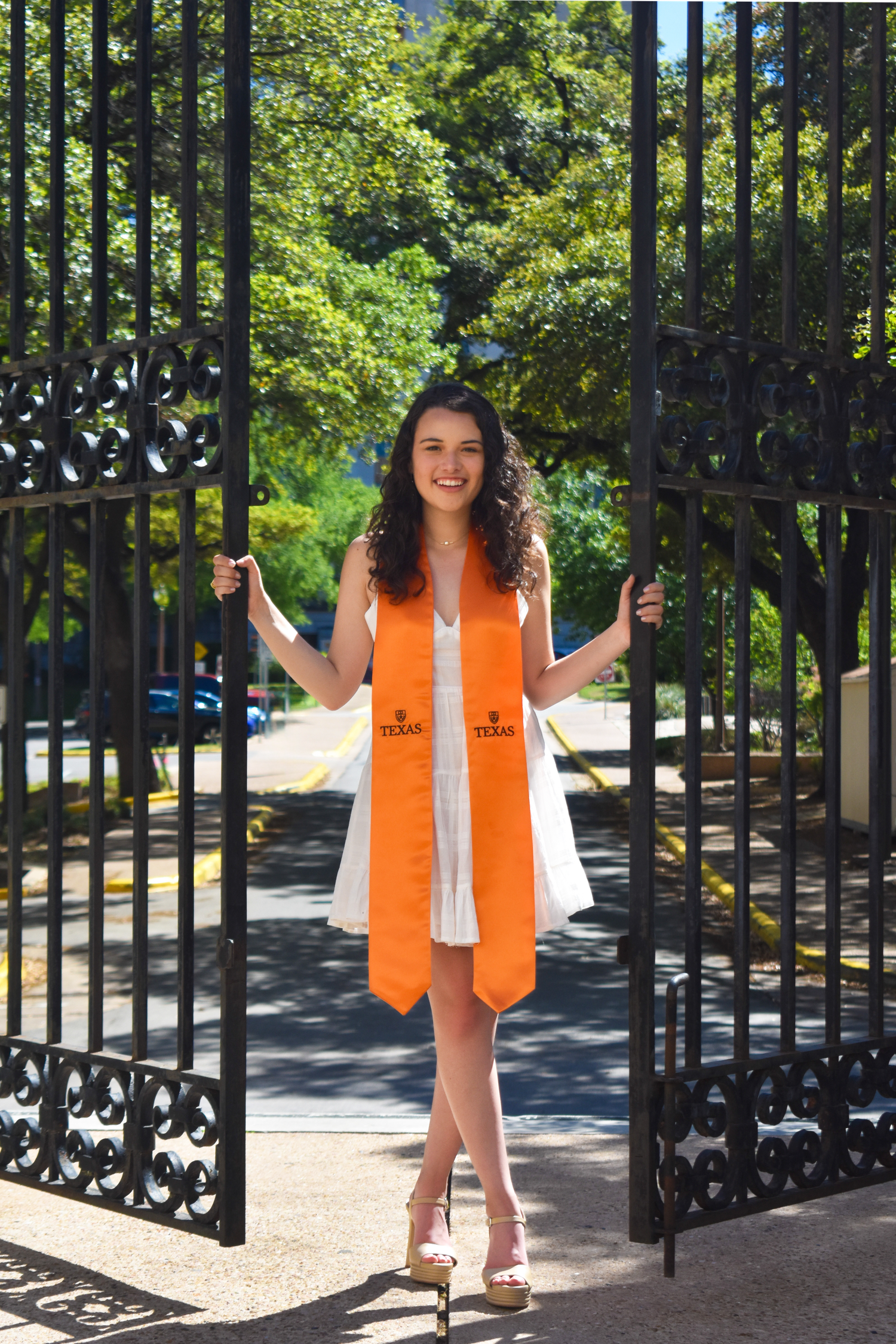 UT Austin graduation portrait at campus iron gates with orange Texas stole