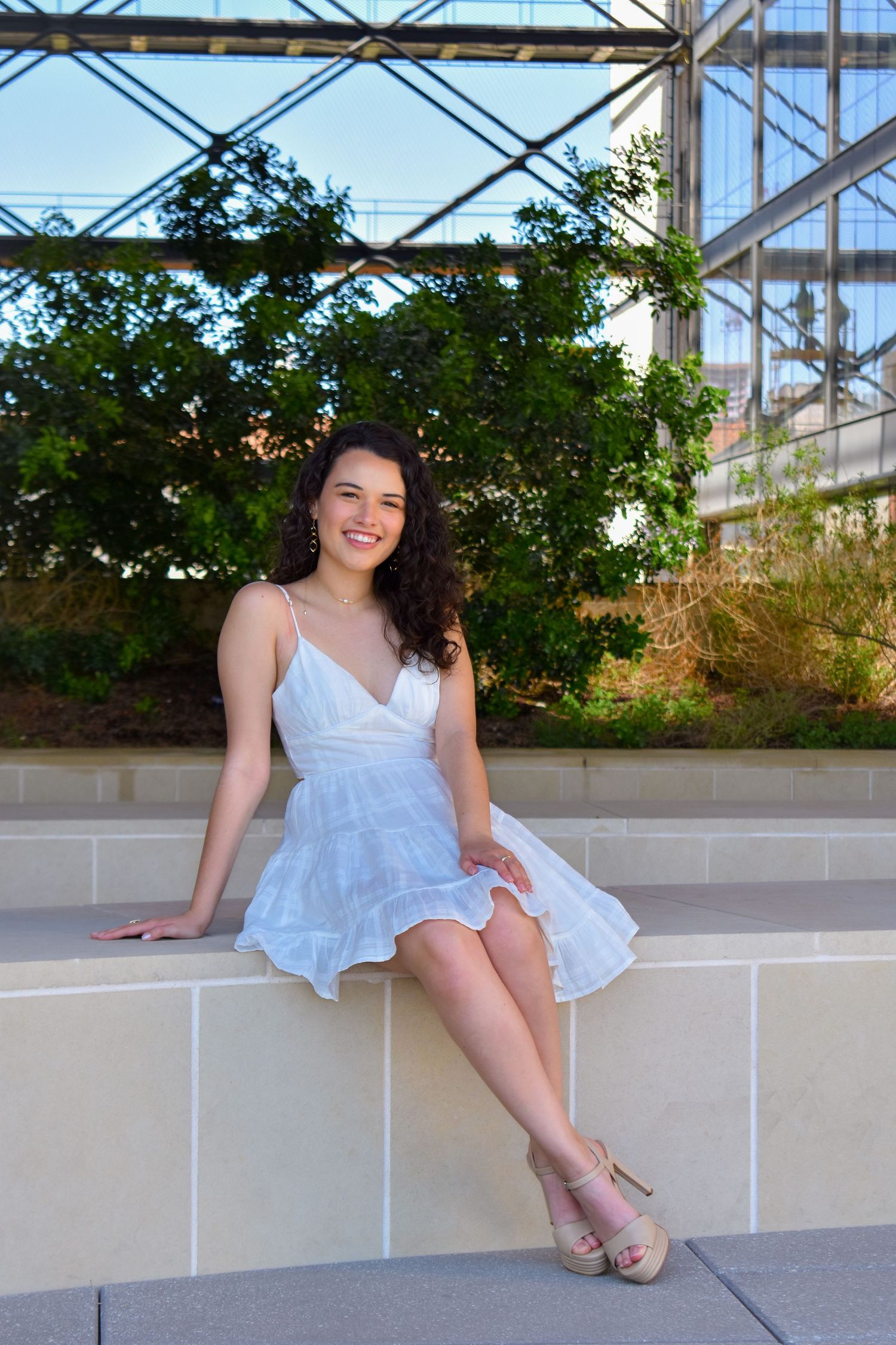 UT Austin graduation portrait of graduate in white dress seated outdoors on campus