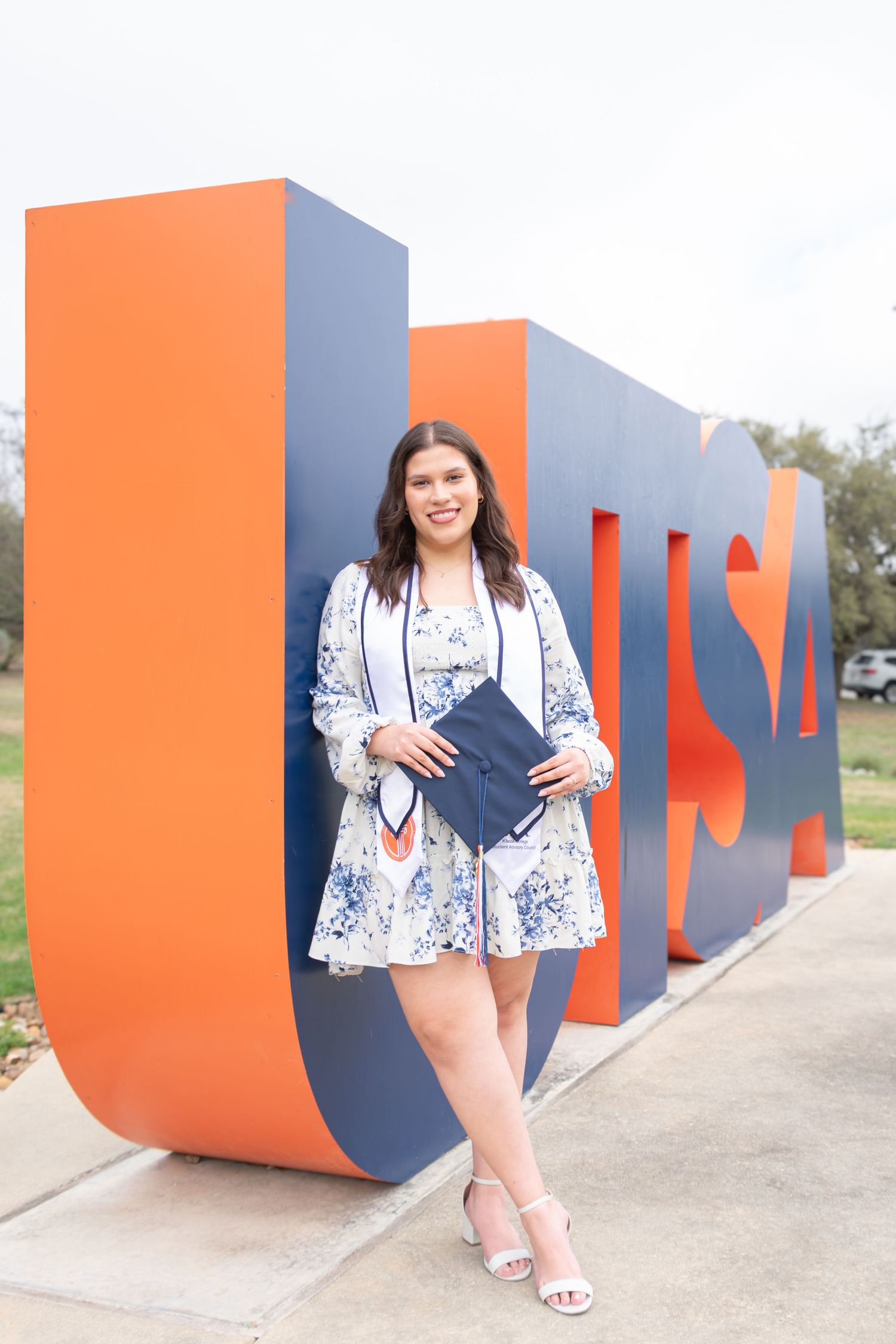 UTSA graduation portrait at the UTSA letter sculptures in San Antonio holding diploma in floral dress