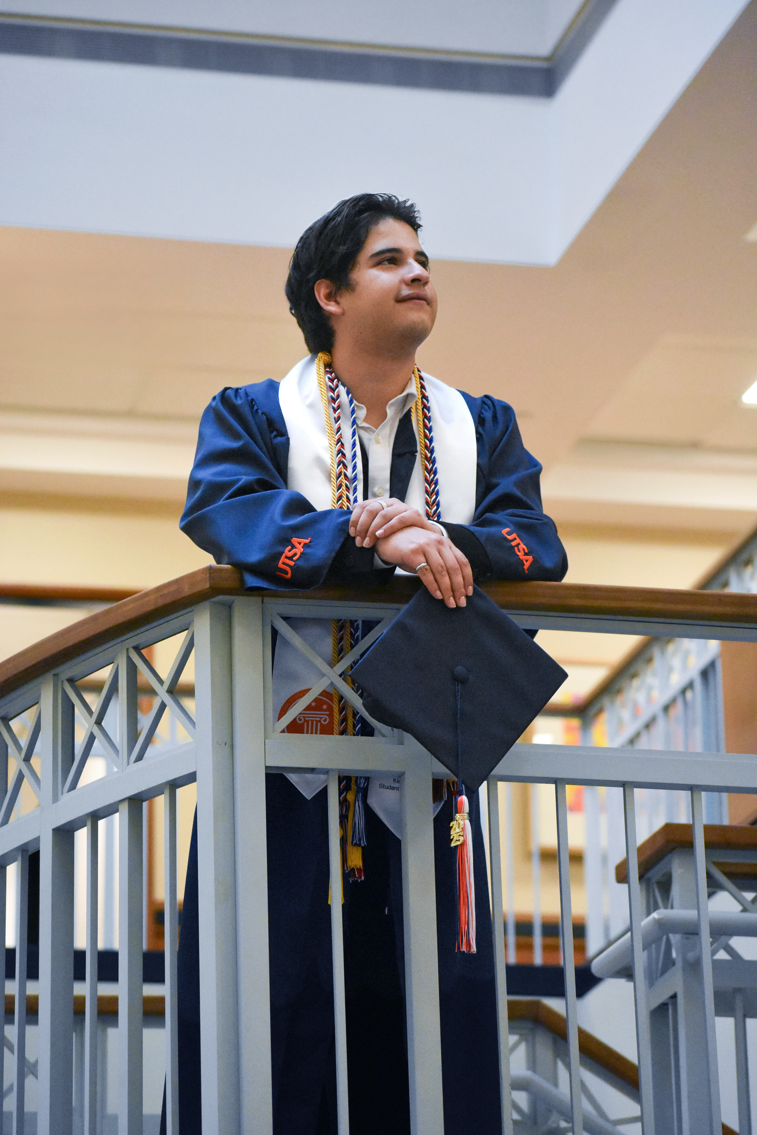 UTSA graduation portrait on campus balcony in cap gown and honor cords in San Antonio