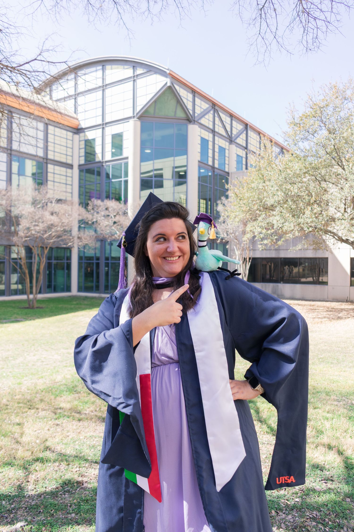 UTSA graduation portrait by the Student Union building in cap and gown with diploma and stole