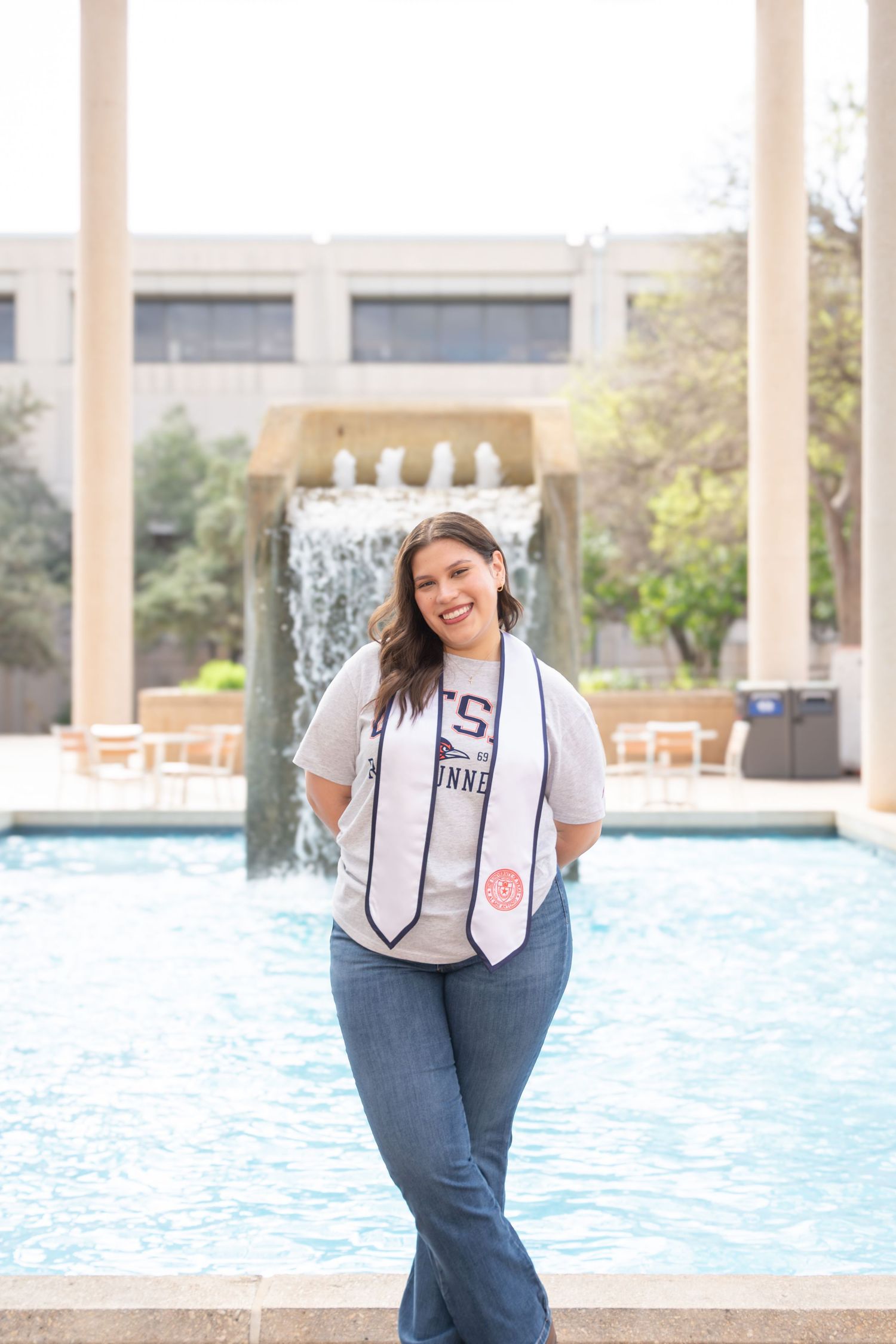 UTSA graduation portrait at the Sombrilla fountain in San Antonio wearing graduation stole