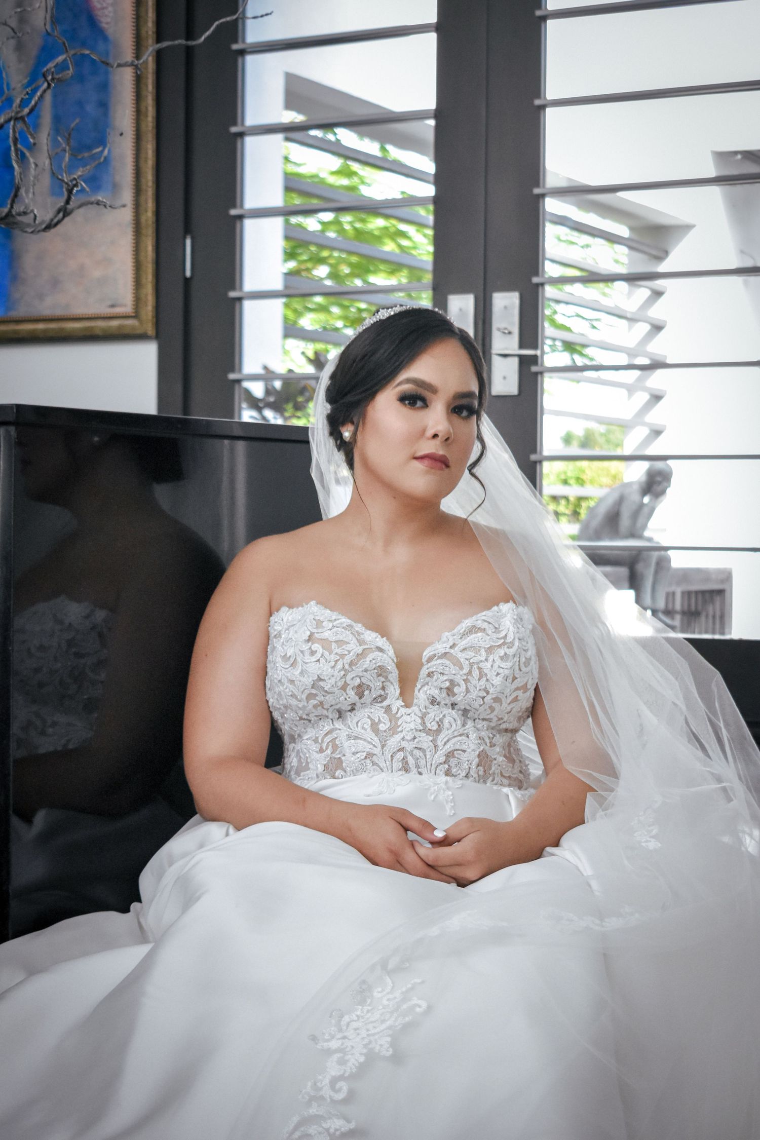 Bridal portrait in Brownsville Texas with bride in lace gown and veil seated by window