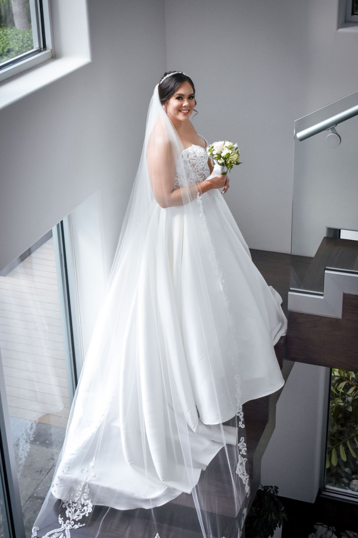 Bridal portrait in Brownsville Texas with bride in flowing gown and veil on staircase with bouquet