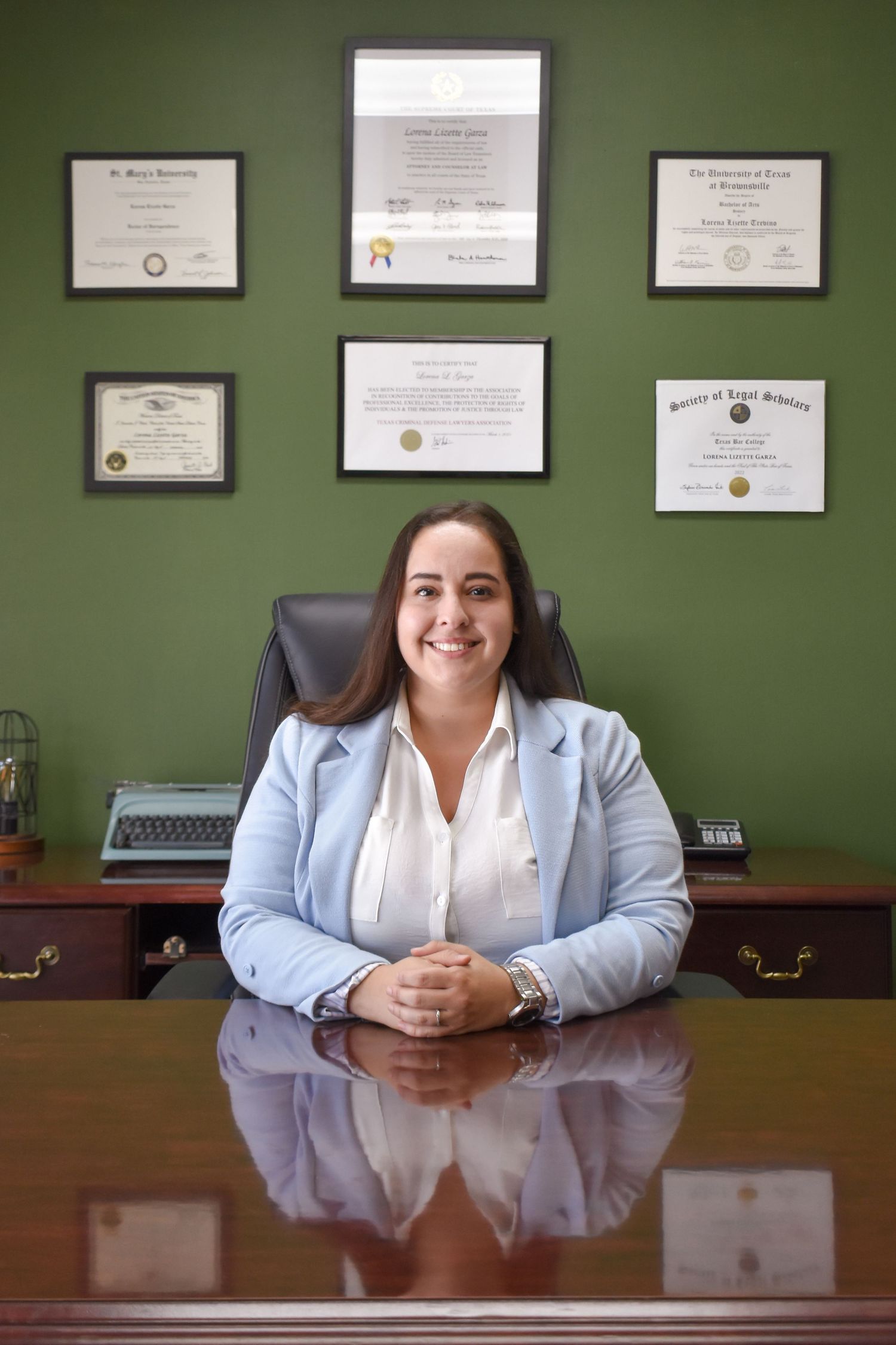 Professional office portrait of San Antonio lawyer at desk with framed credentials on wall
