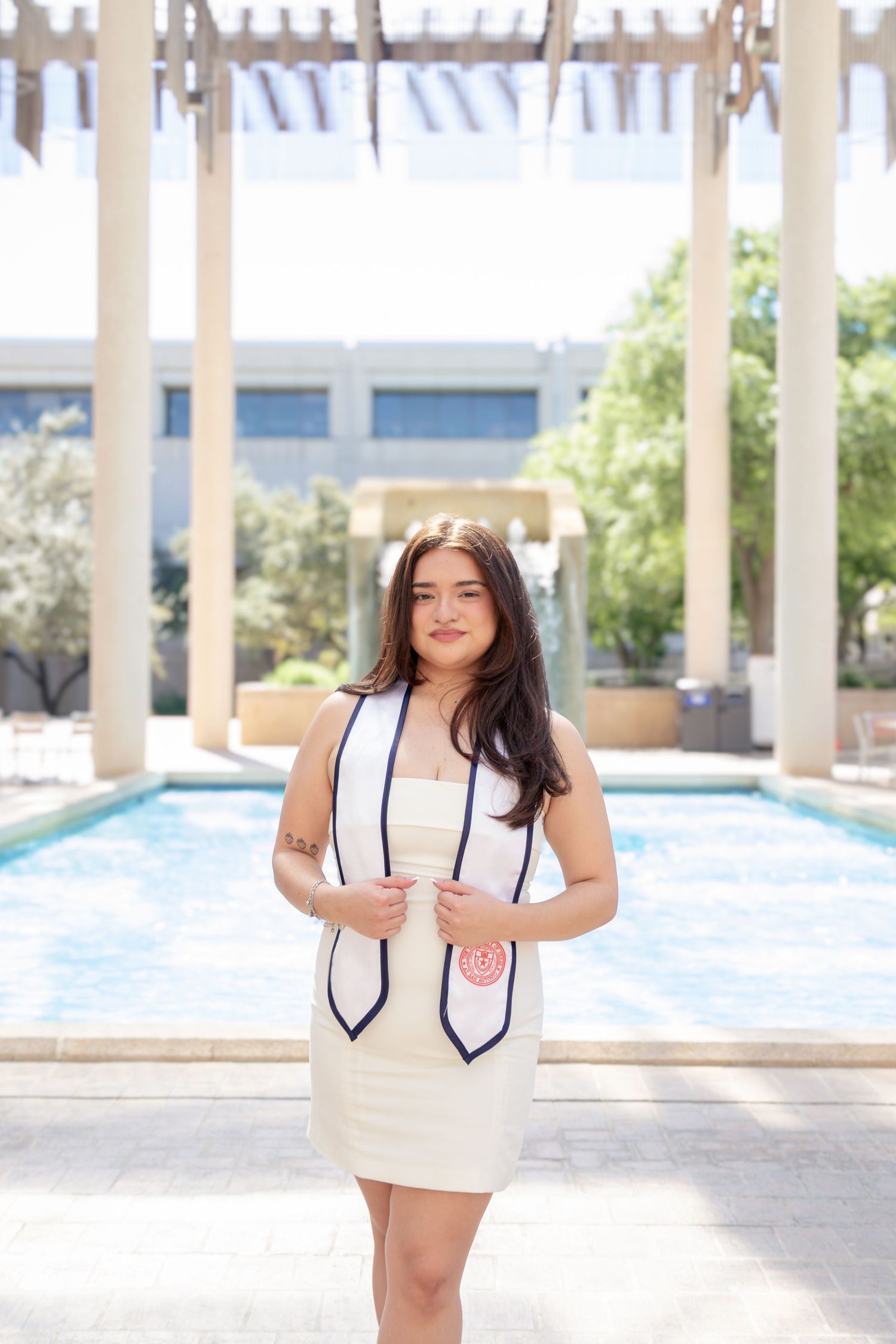 UTSA graduation portrait at the Sombrilla fountain in San Antonio wearing graduation stole