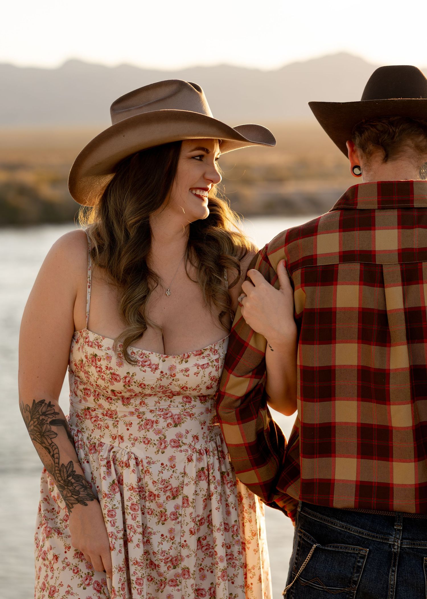 Woman in floral dress and cowboy hat smiling at her partner during a golden hour photoshoot.