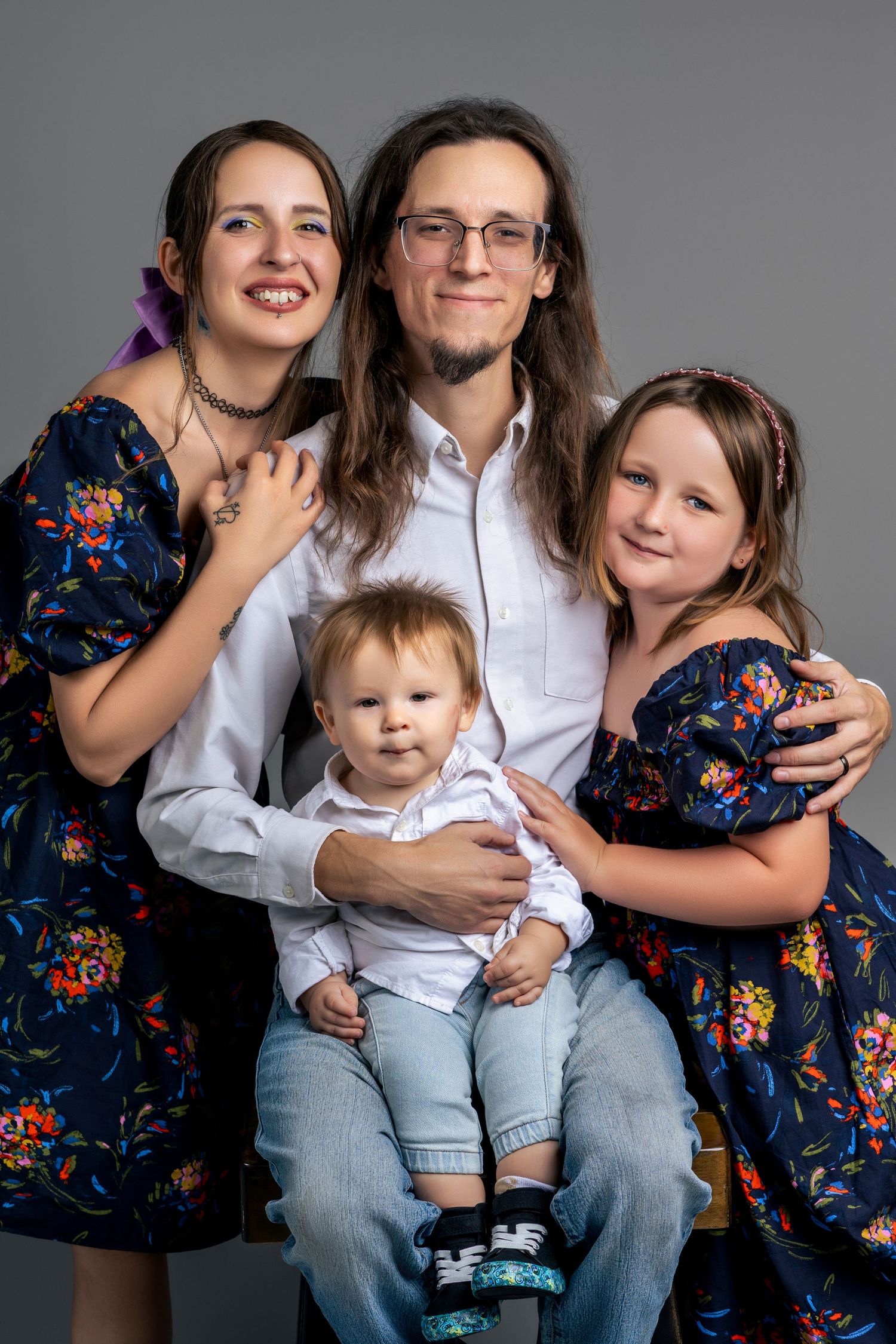 A happy family of four poses in a studio, including parents, a young girl, and a baby.