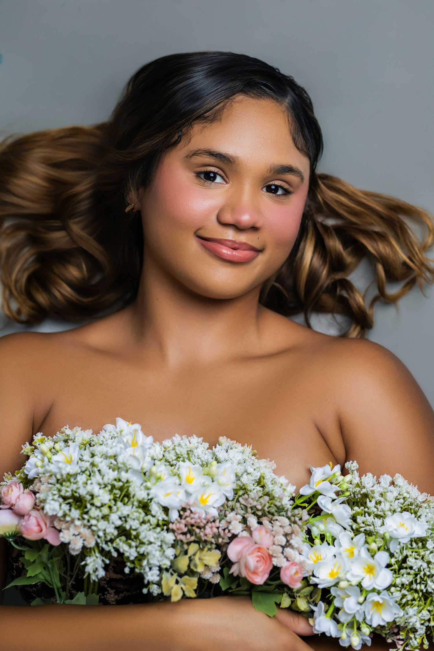 A smiling young woman holds a bouquet of white and pink flowers with flowing wavy hair.
