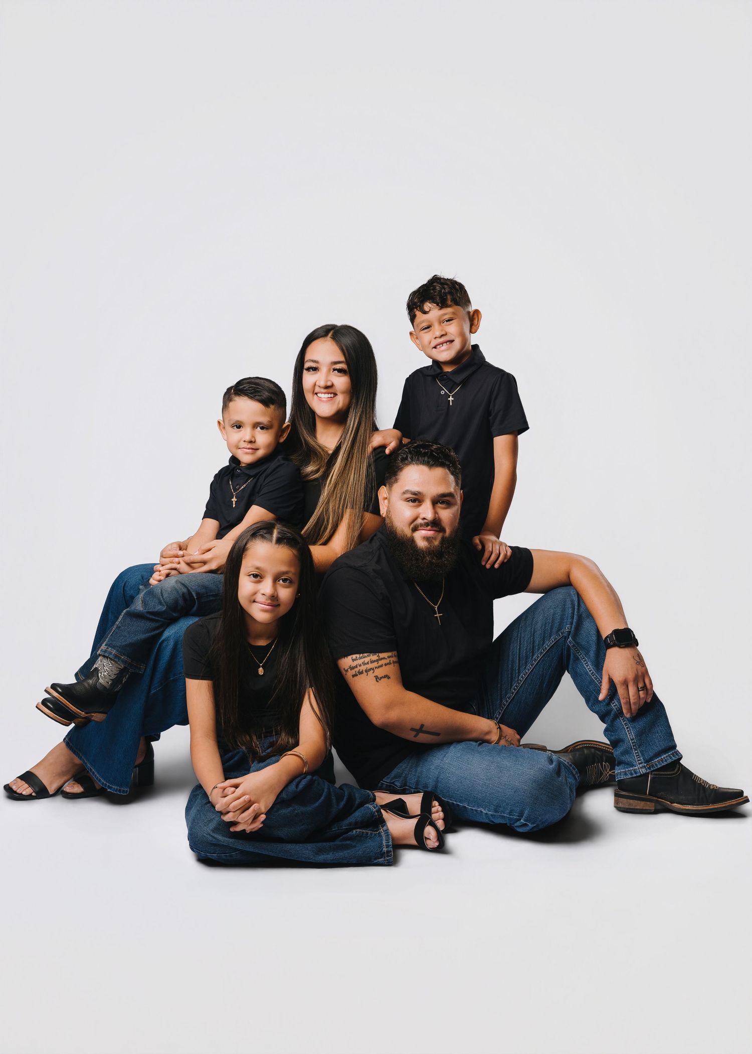 Family of five posing in matching black outfits and jeans against a white studio background.