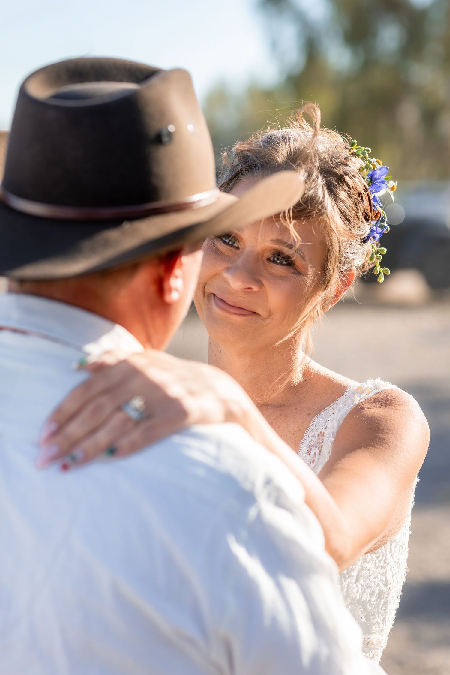 Bride with floral hair accessories gazing lovingly at groom in cowboy hat outdoors.