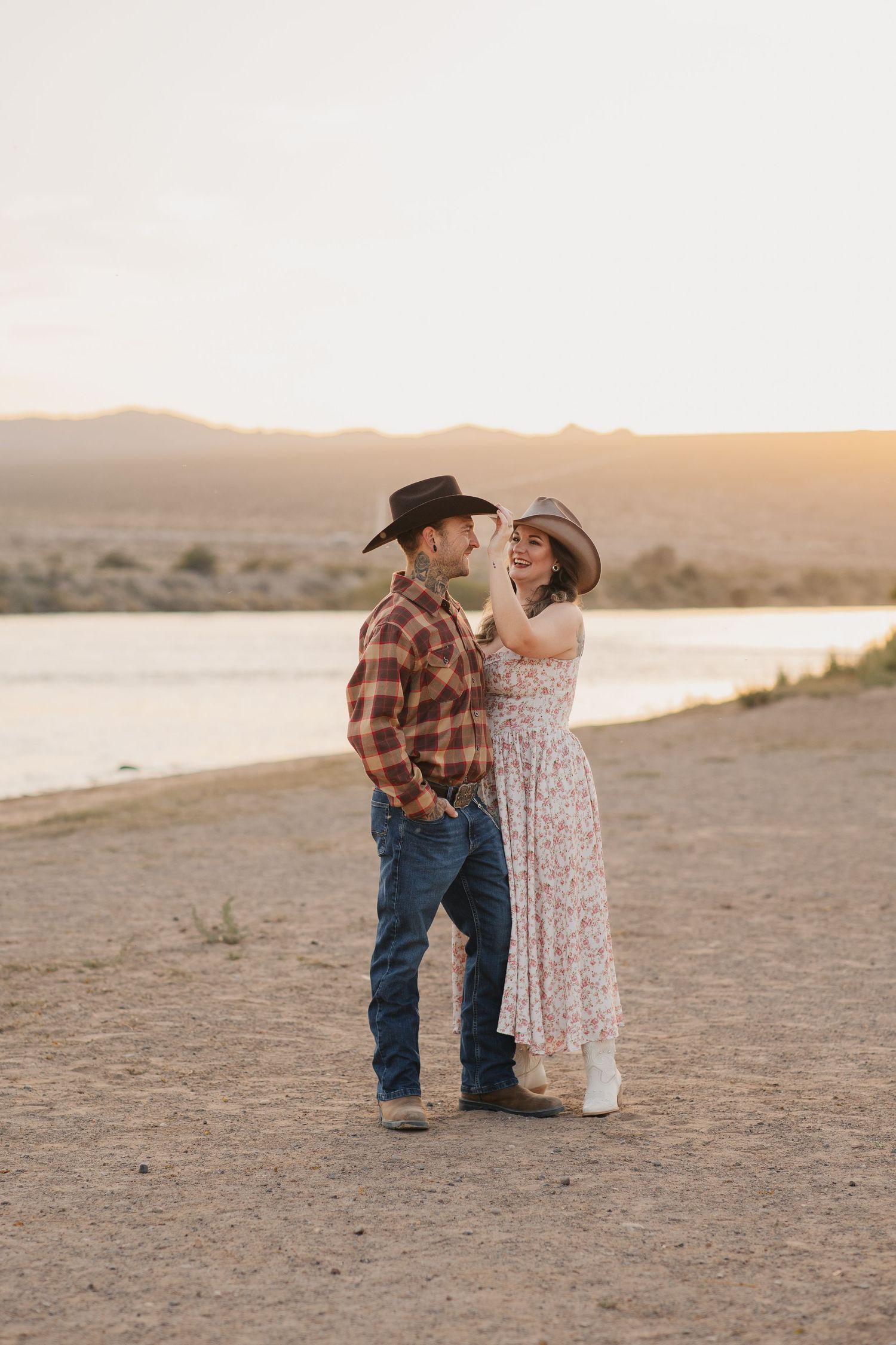 Couple in western wear sharing a romantic moment at sunset near a river.