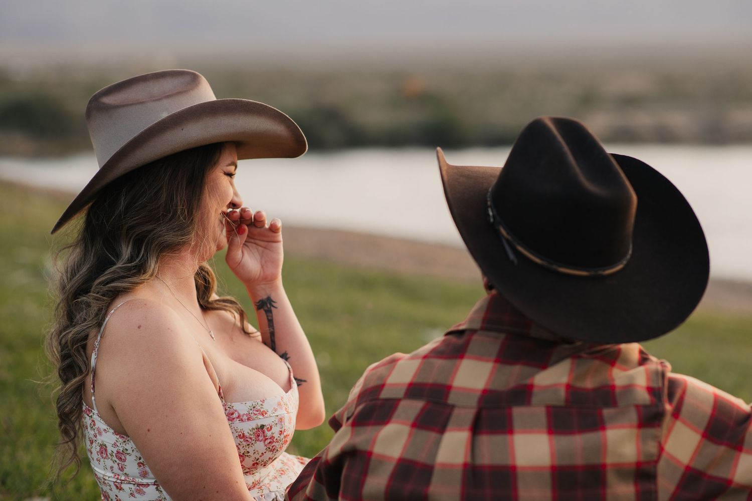 Couple in cowboy hats sharing a romantic moment by a river at golden hour.