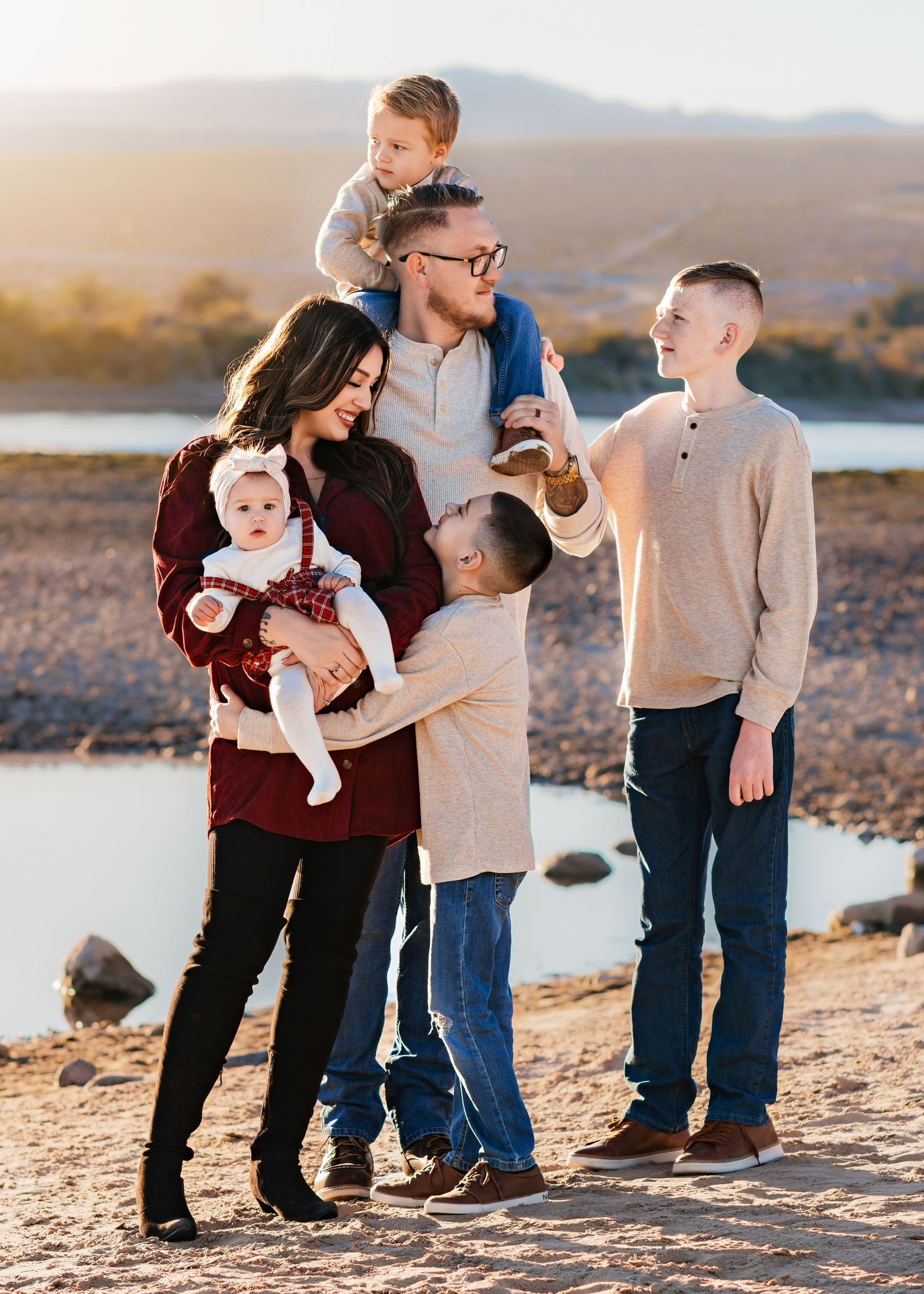 Happy family with four children poses together on rocky desert landscape near lake at sunset.