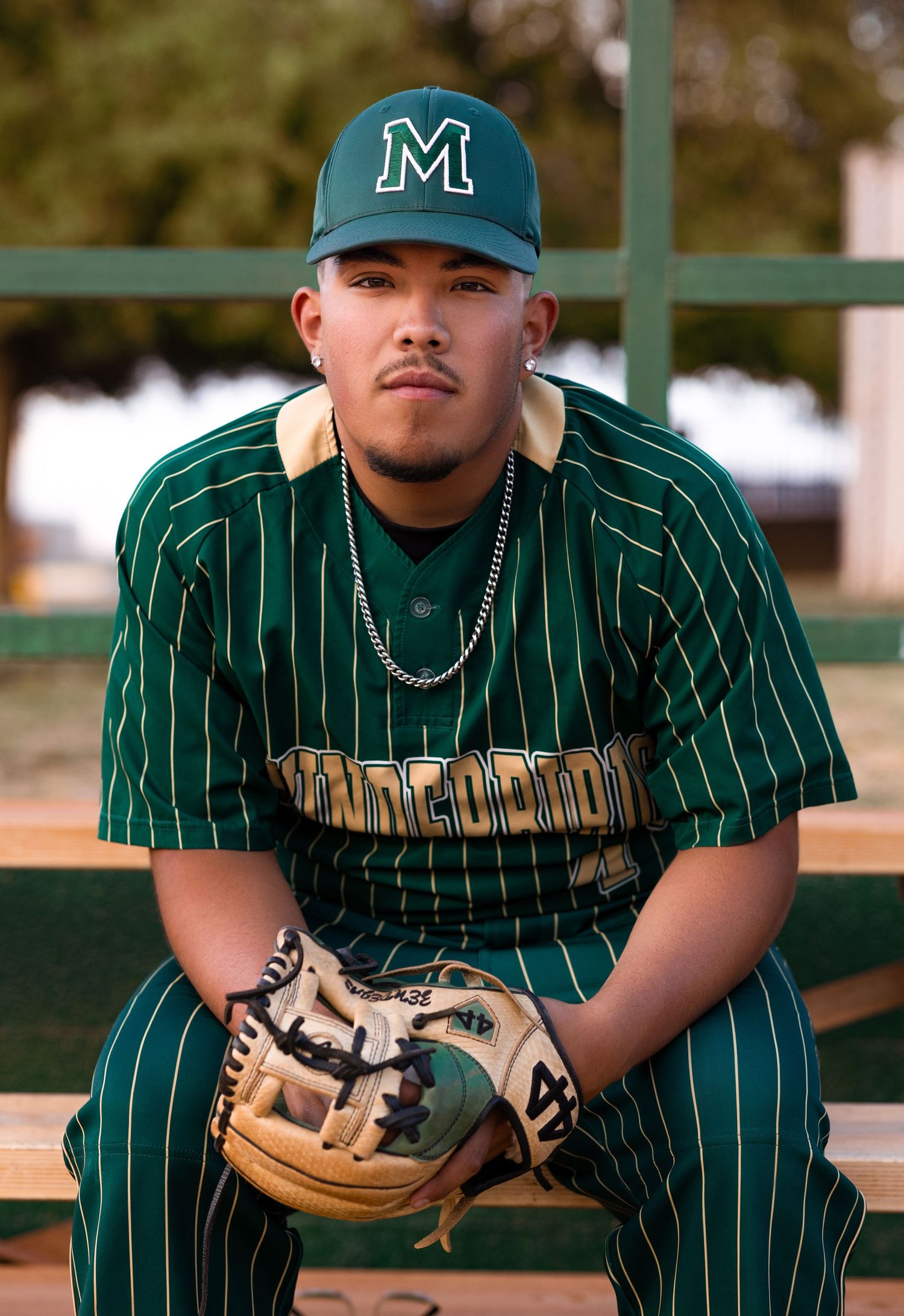 Young baseball player in green Thunderbirds pinstripe uniform sitting on bleachers with glove.