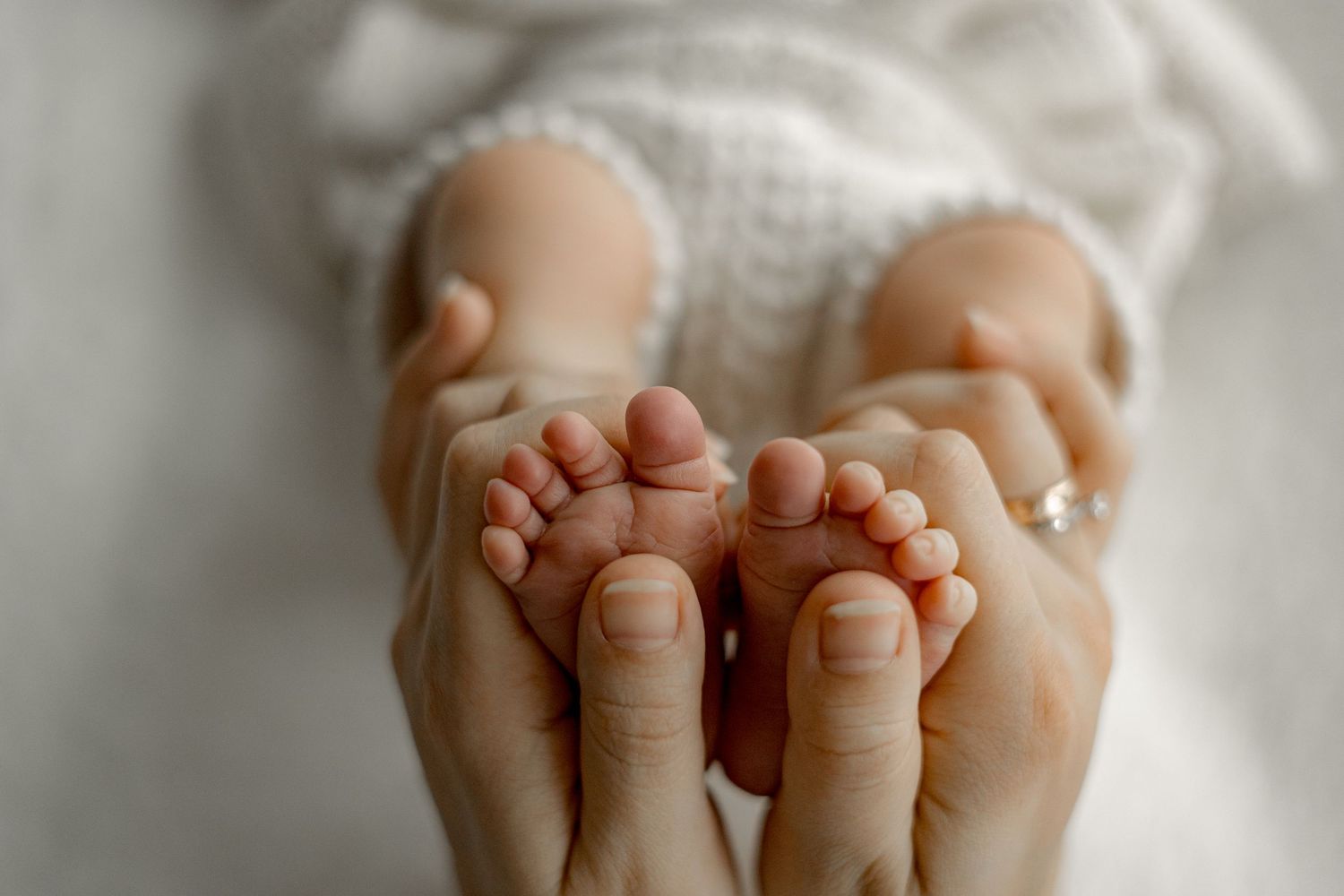 Close-up of a parent's hands gently cradling tiny newborn baby feet wrapped in a soft white blanket.